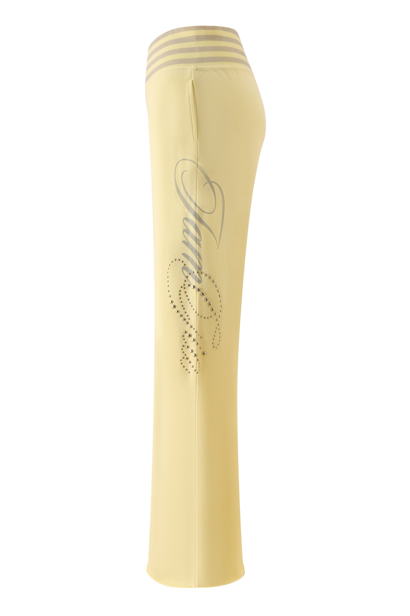 Side view of the I.AM.GIA VEDA PANT - YELLOW, a light yellow low-rise track pant featuring a silver script design and rhinestone embellishments on the upper leg. The waistband showcases three horizontal stripes, while the wide-leg silhouette provides a relaxed fit.