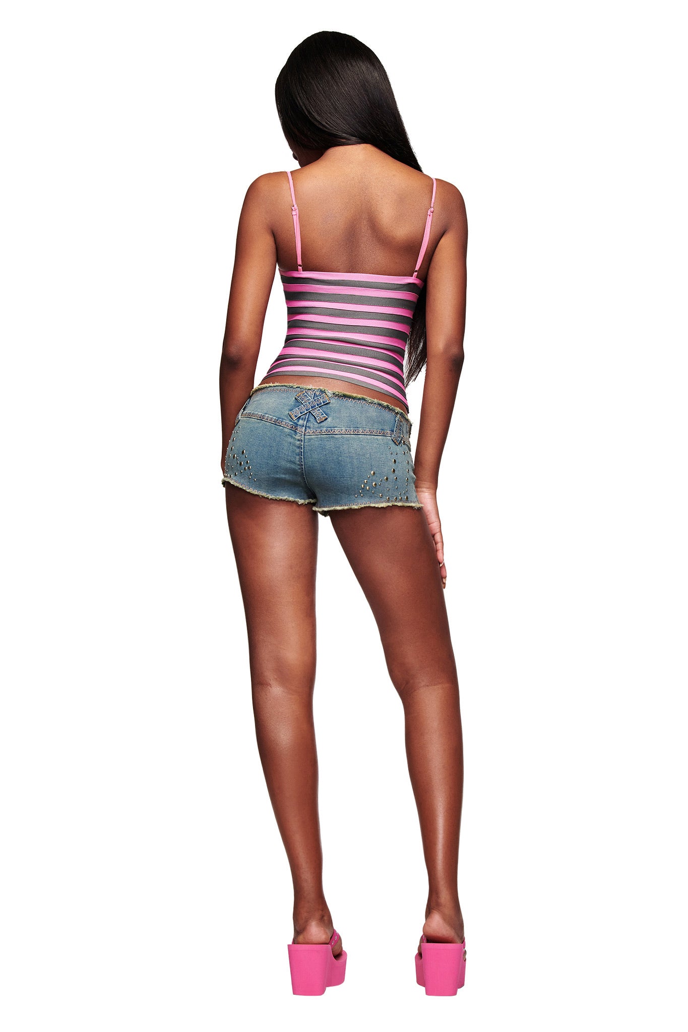 A woman faces away, wearing the I.AM.GIA NYNA BANDAGE CAMI TOP in hot pink, styled with frayed denim shorts and pink platform heels. She has long straight hair and stands against a white background.