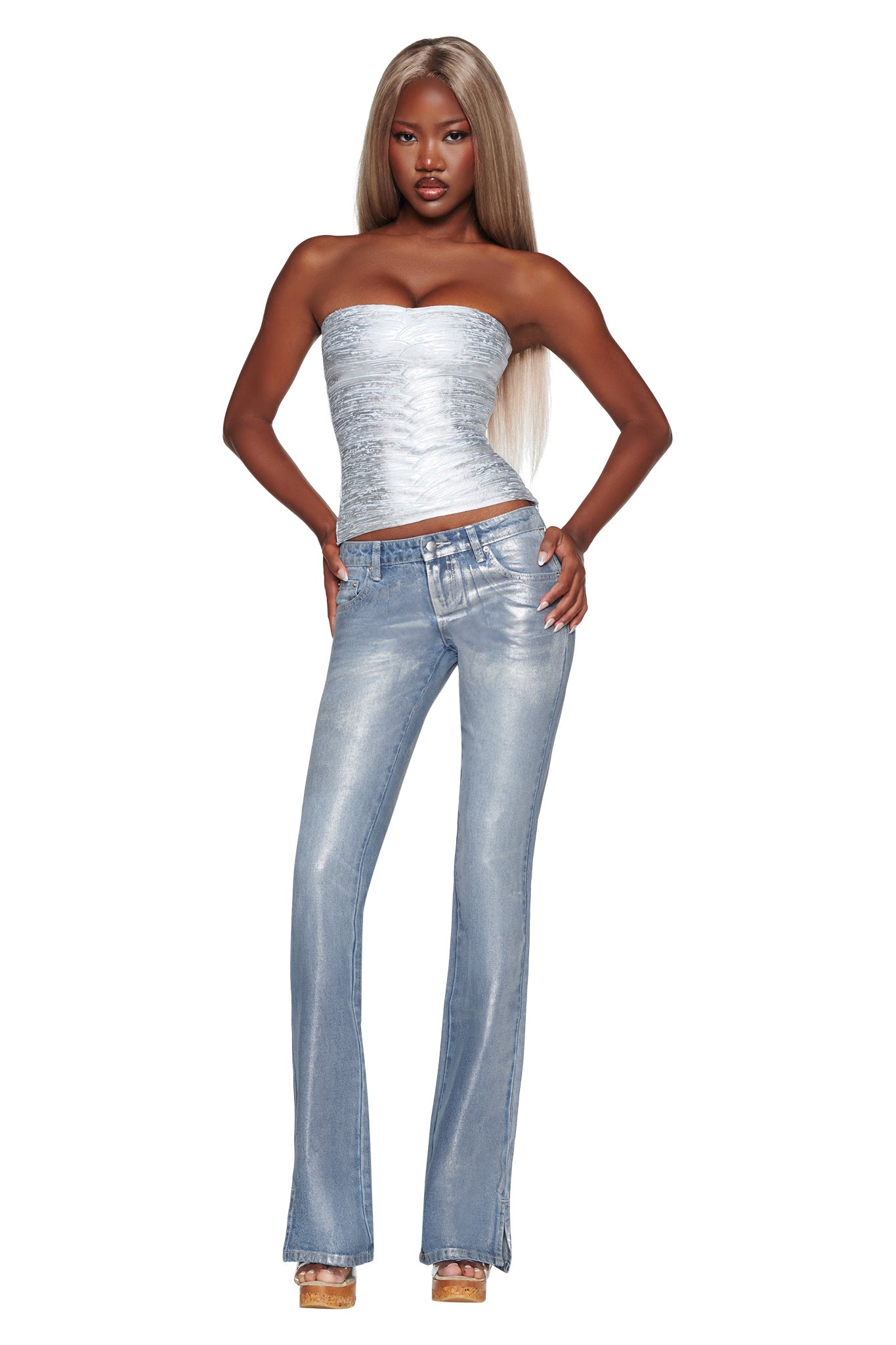 A woman with long blonde hair poses against a white background wearing the I.AM.GIA KHIA BANDAGE BOOB TUBE in Metallic Blue, styled with light blue flared jeans and platform heels, one hand on her hip.