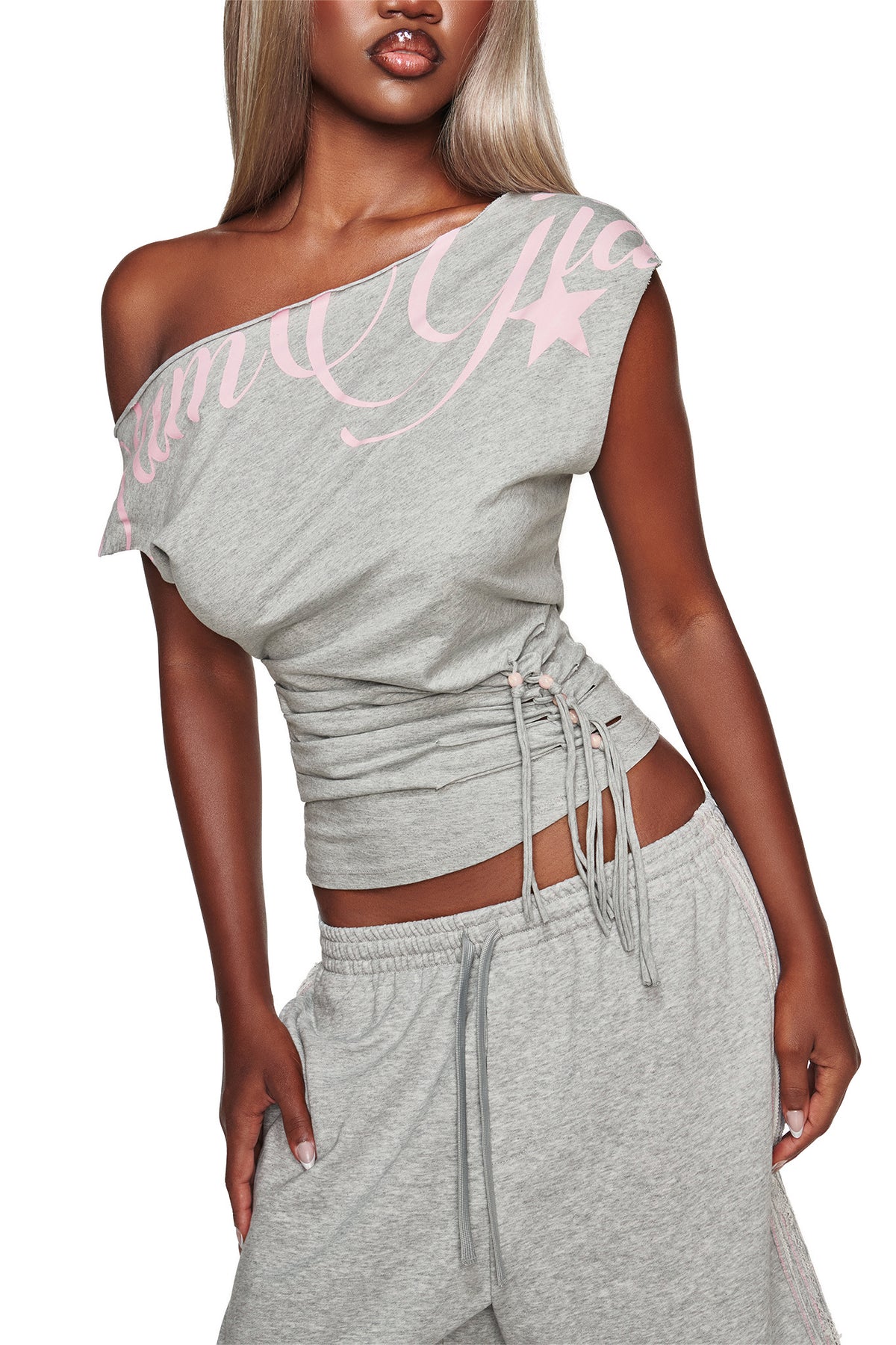 A woman poses with one hand on her hip, wearing the I.AM.GIA BEX OFF SHOULDER TOP in grey marle with pink script, paired with matching drawstring pants.