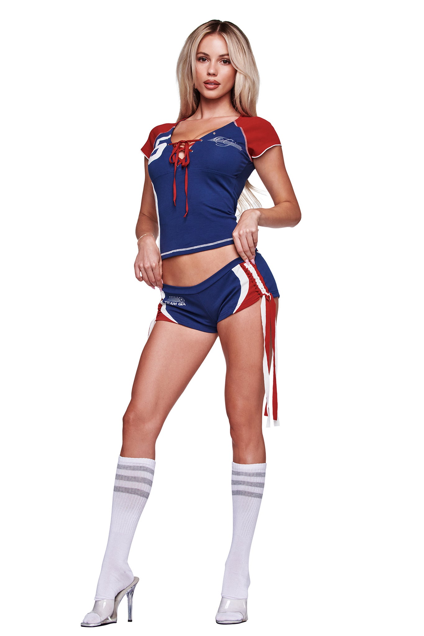 A woman poses against a white background wearing I.AM.GIA's NOVIA MICRO SPORT SHORT in navy, styled with knee-high white socks and high-heeled shoes for a sporty look.