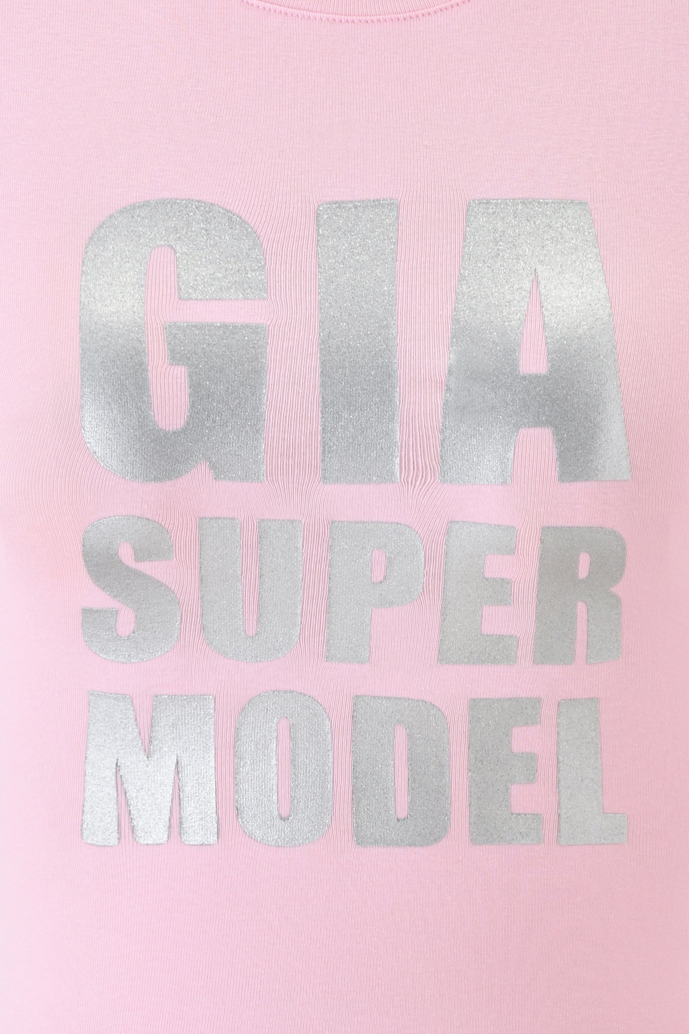 Close-up of the COURTNEY TANK - SUPER MODEL by I.AM.GIA, a baby pink muscle tank with "GIA SUPER MODEL" in large, metallic silver letters on the front.