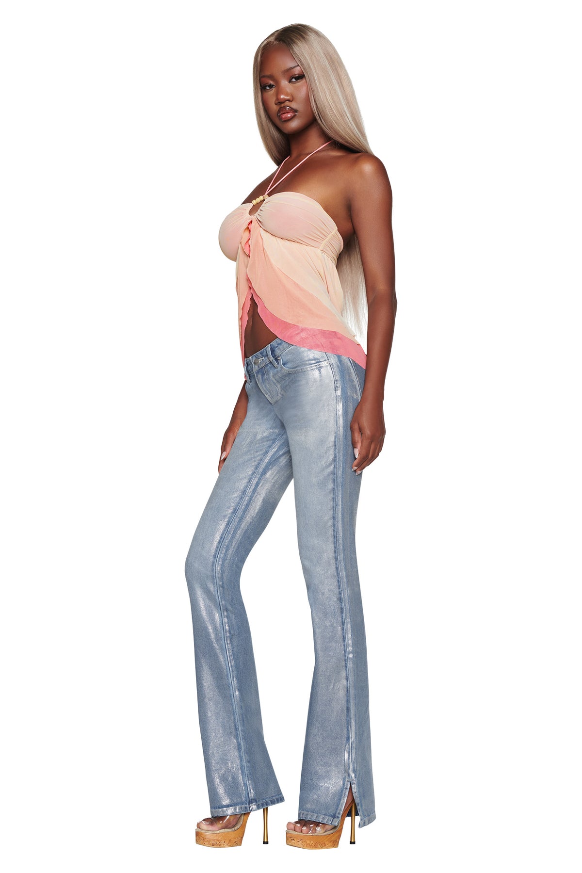 A woman with long blonde hair wears the I.AM.GIA IDALIA TOP in Raspberry Multi, featuring peach and pink tones with multi-colour ruffles, styled with light blue flared jeans and tan platform heels, standing against a white background.