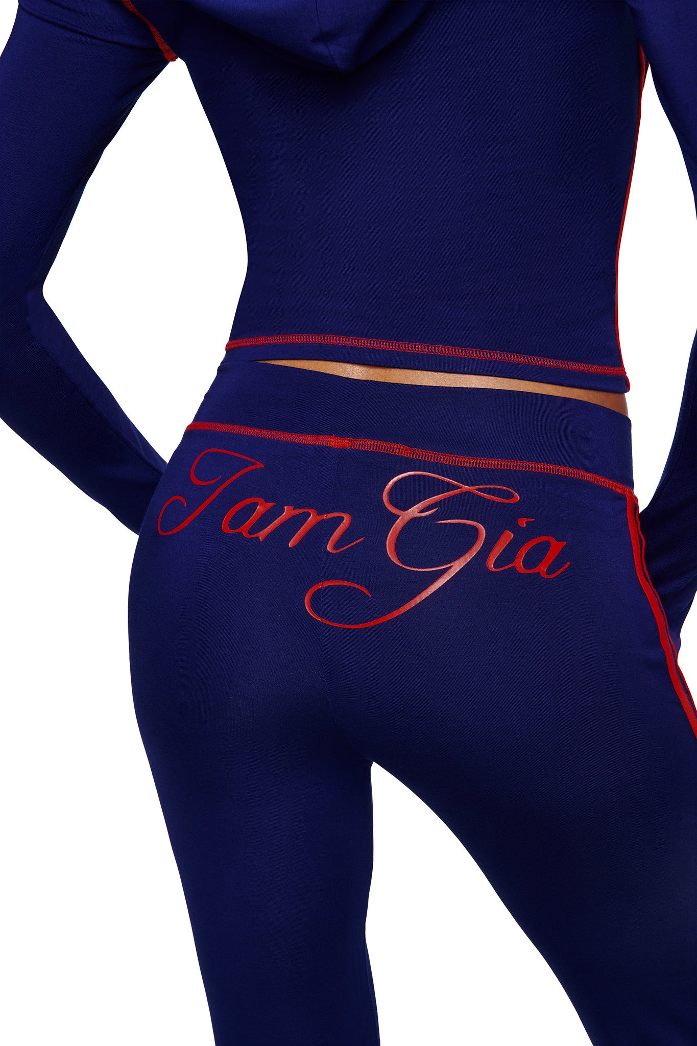 A person wears I.AM.GIA's BLARE SPORT TRACKPANT in navy with red trim; the buttery-soft fabric stands out, featuring "I.AM.GIA" in bold red script across the back.