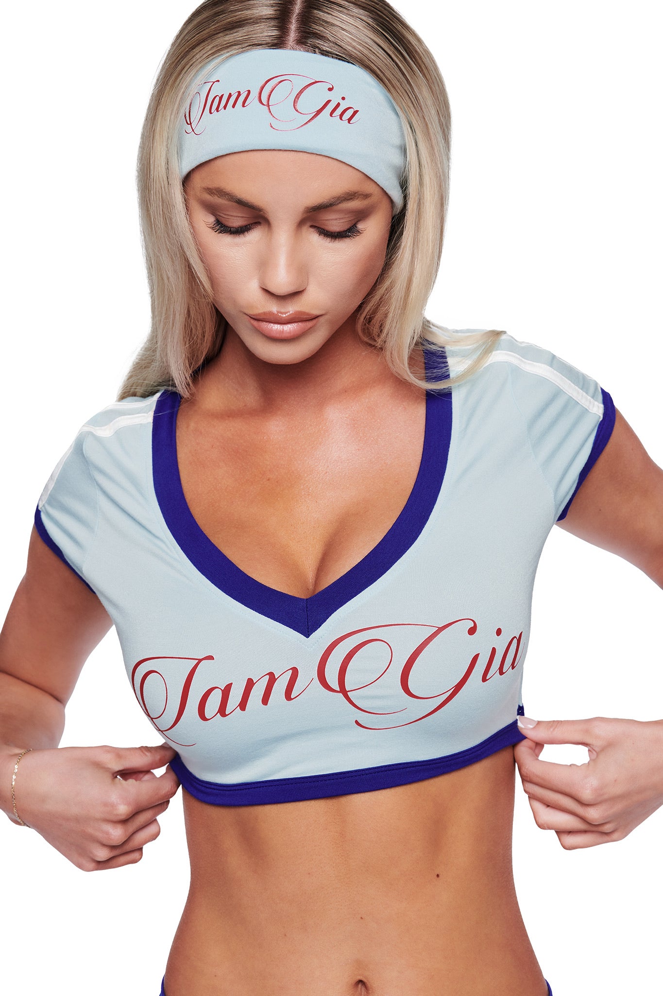 A woman with long blonde hair wears the I.AM.GIA BLARE SPORT HEADBAND in baby blue, adjusting her top while looking downward against a white background.