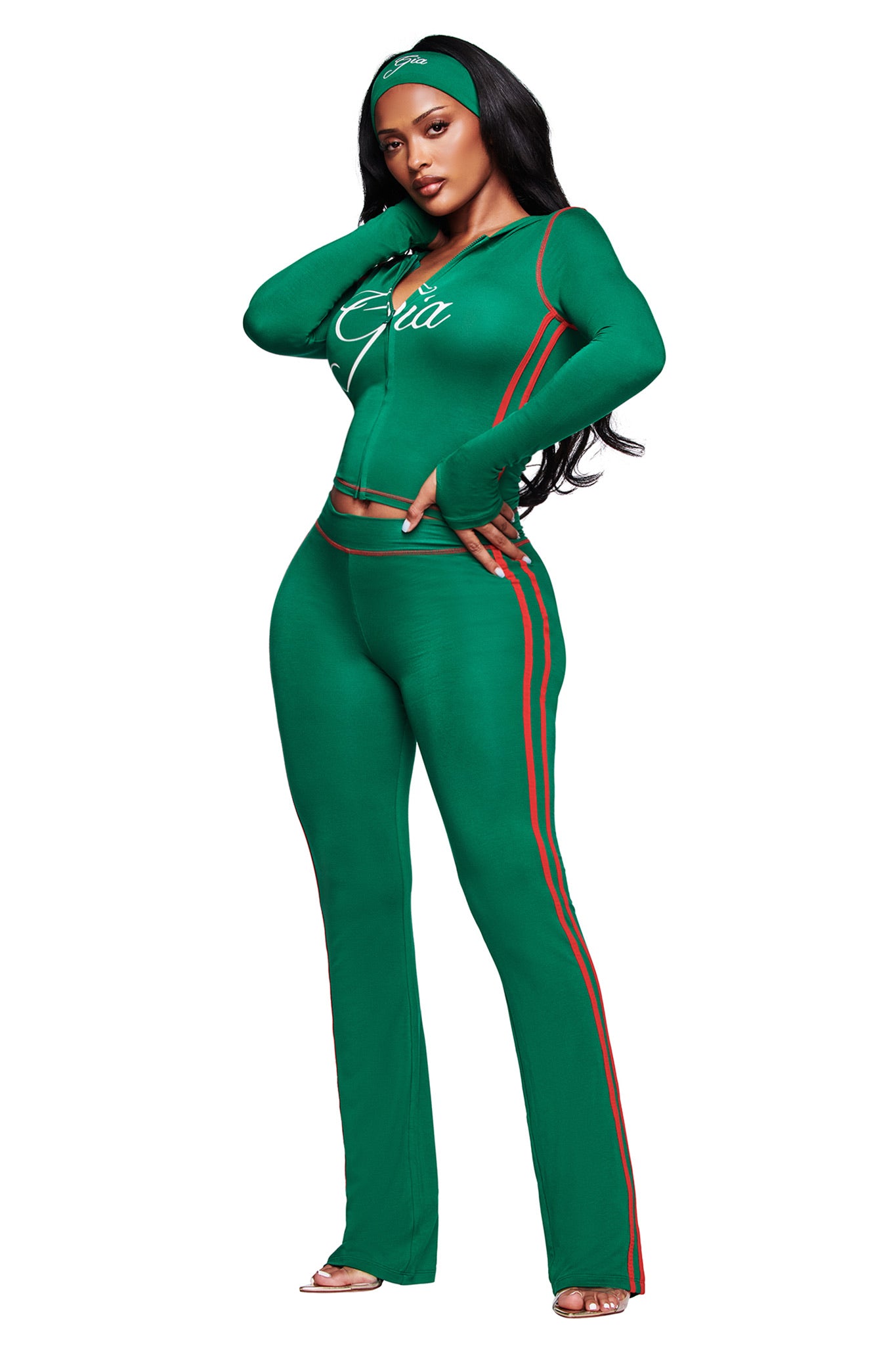A woman exudes confidence in a fitted green tracksuit with red stripes and high heels, styled with the I.AM.GIA BLARE SPORT HEADBAND - GREEN for a look that merges sporty flair and elegance.