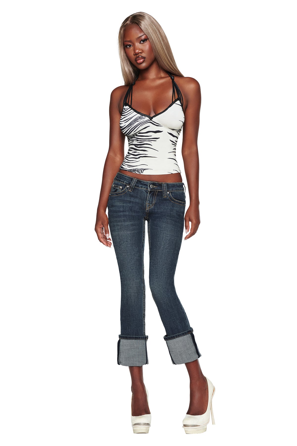 A woman with long blonde hair wears a zebra-print top, I.AM.GIA’s BIANKA JEAN in blue, and white high heels, standing against a white background.