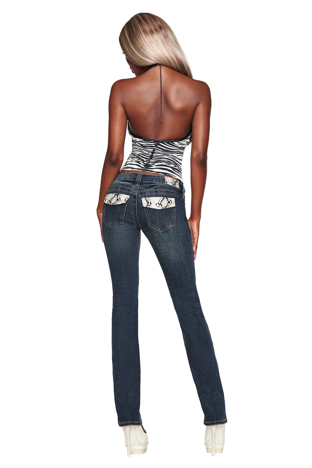 A woman with long blonde hair stands facing away, wearing a zebra print halter top, clear high heels, and the I.AM.GIA BIANKA JEAN in blue featuring slim straight legs and patterned back pockets.