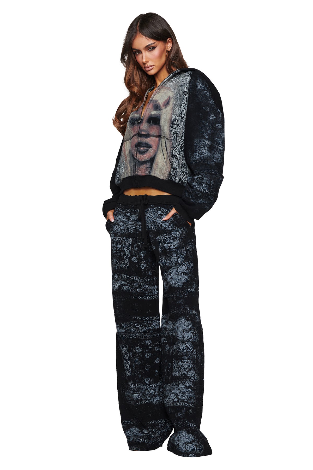 A woman showcases bold street style against a white background, wearing a black and gray bandana-print hoodie featuring a graphic of a blonde woman’s face, paired with I.AM.GIA’s T-REX TRACKPANT in Black Bandana.
