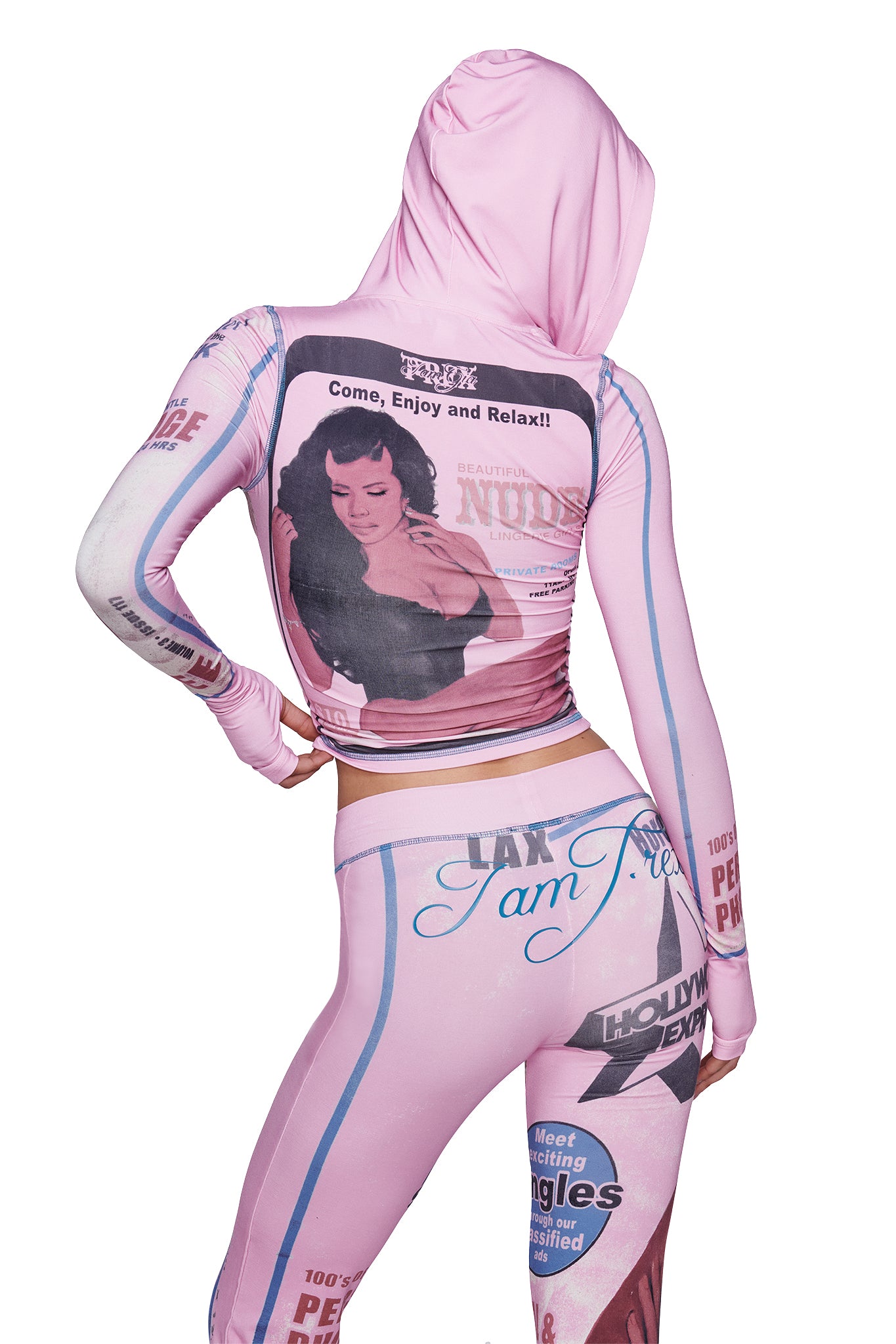 A person wearing the I.AM.GIA T-REX BLARE HOODIE in pink—which showcases eye-catching retro magazine-style graphics, such as a posing woman and bold statements—stands with one hand on their hip, turned away from the camera.