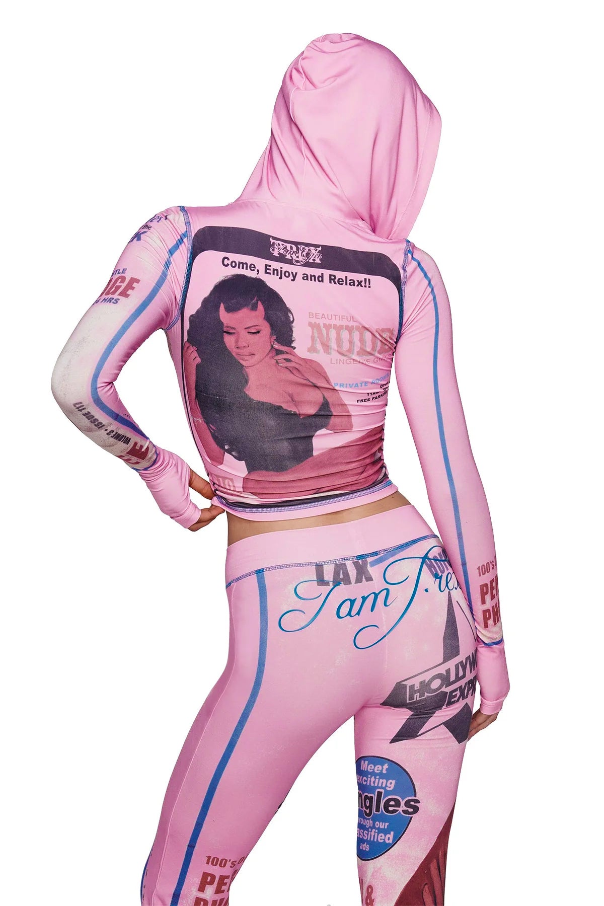 A person is seen from behind and partly in profile, wearing the I.AM.GIA T-REX BLARE HOODIE in pink—a bamboo-fabricated hoodie featuring vintage magazine-inspired prints, including a woman's image and assorted text.