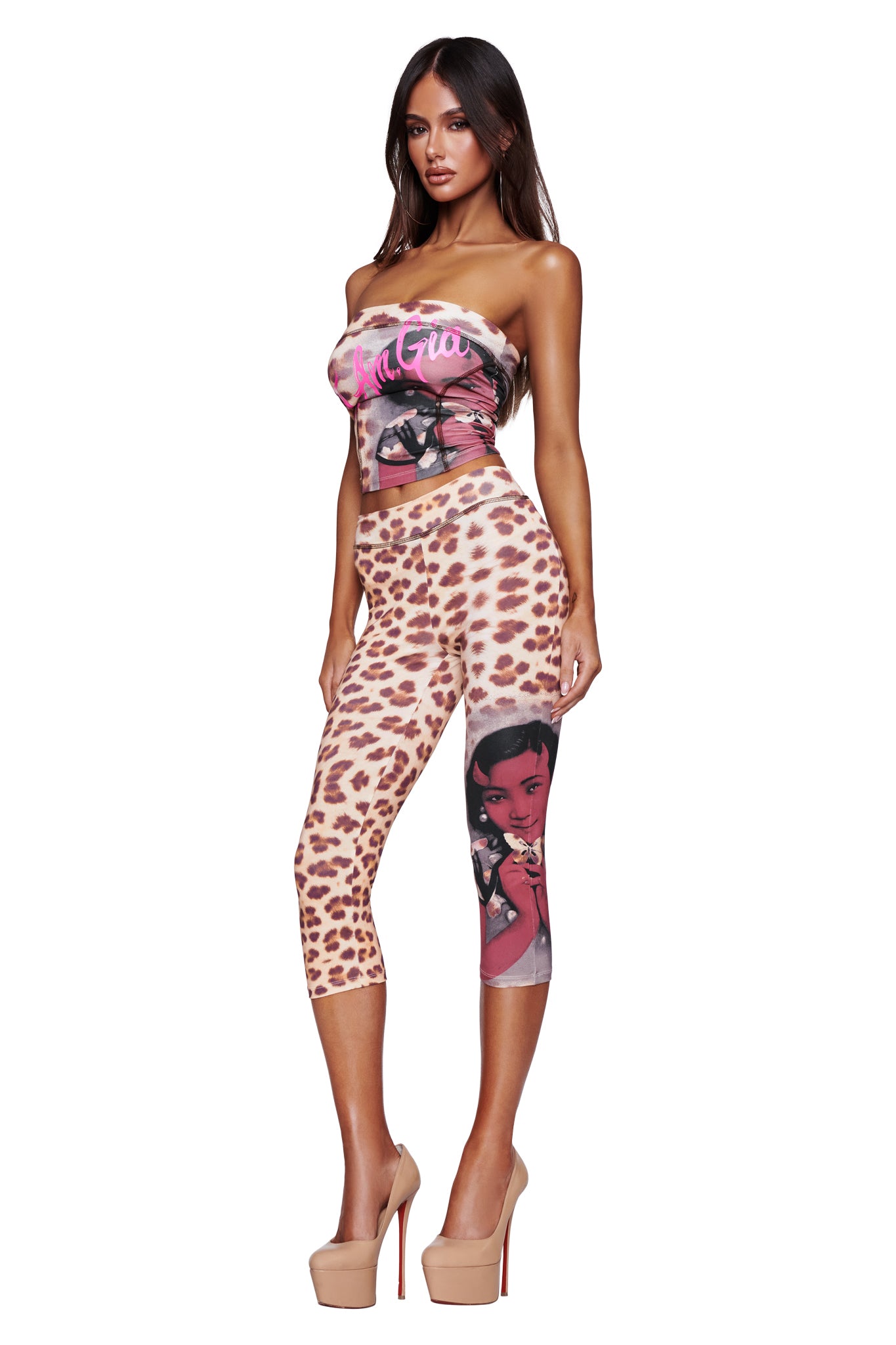 A woman in high heels wears a strapless graphic print top and the I.AM.GIA T-REX BLARE CAPRI - WILD CARD, featuring cheetah print and a comic-style illustration on one leg, while posing against a white background.