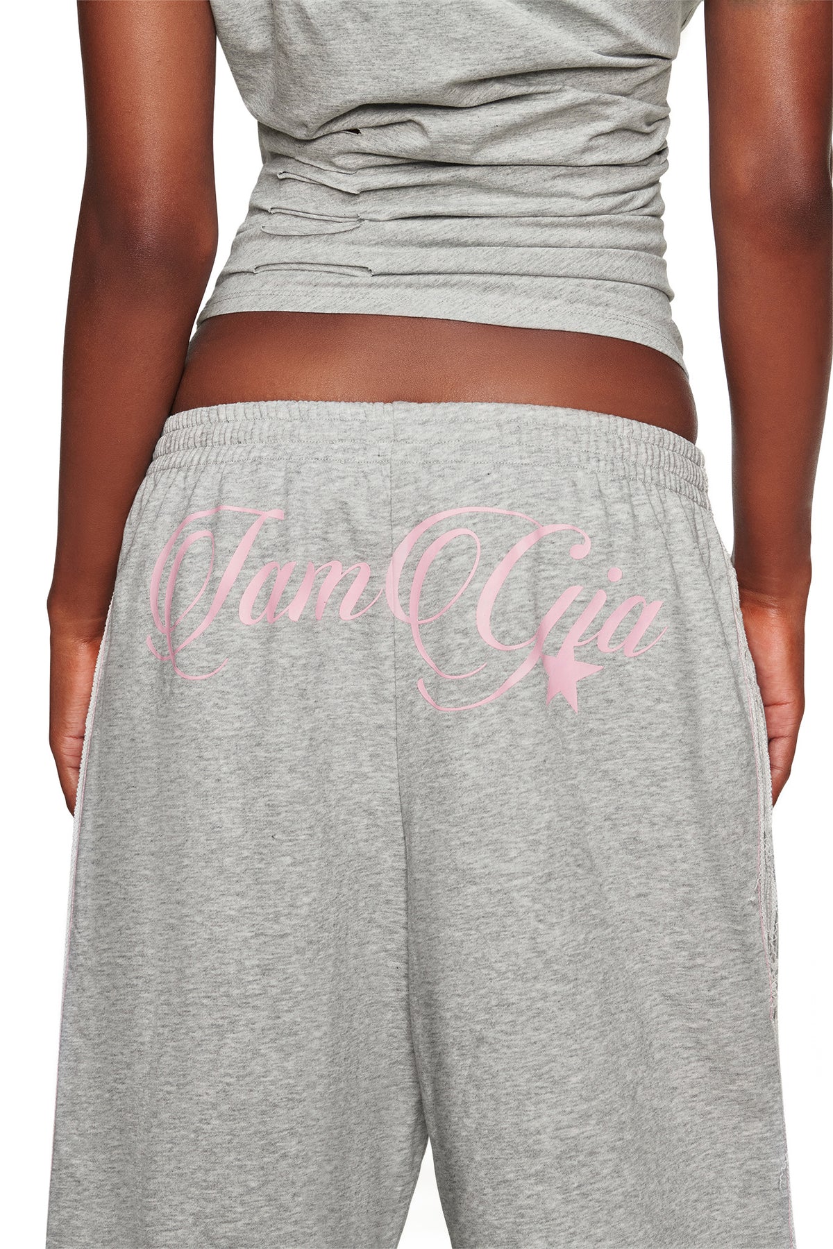 A person wearing the I.AM.GIA BEX TERRY SHORT in grey, which features pink cursive “I.AM.GIA” lettering across the back and an elasticated waistband for a relaxed fit, shown from behind.