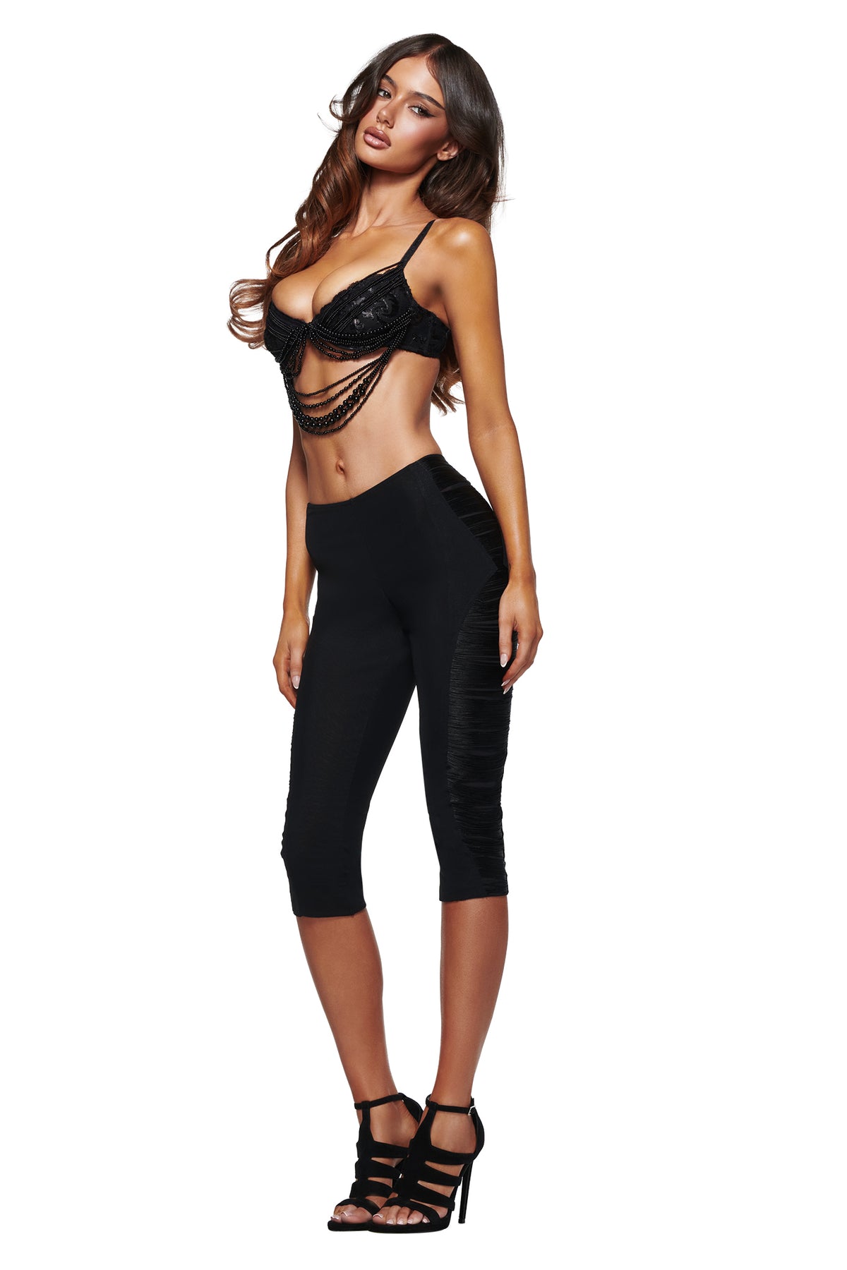 A woman poses against a white background wearing the I.AM.GIA VERON BRA in black, styled with black cropped leggings and black high heels.
