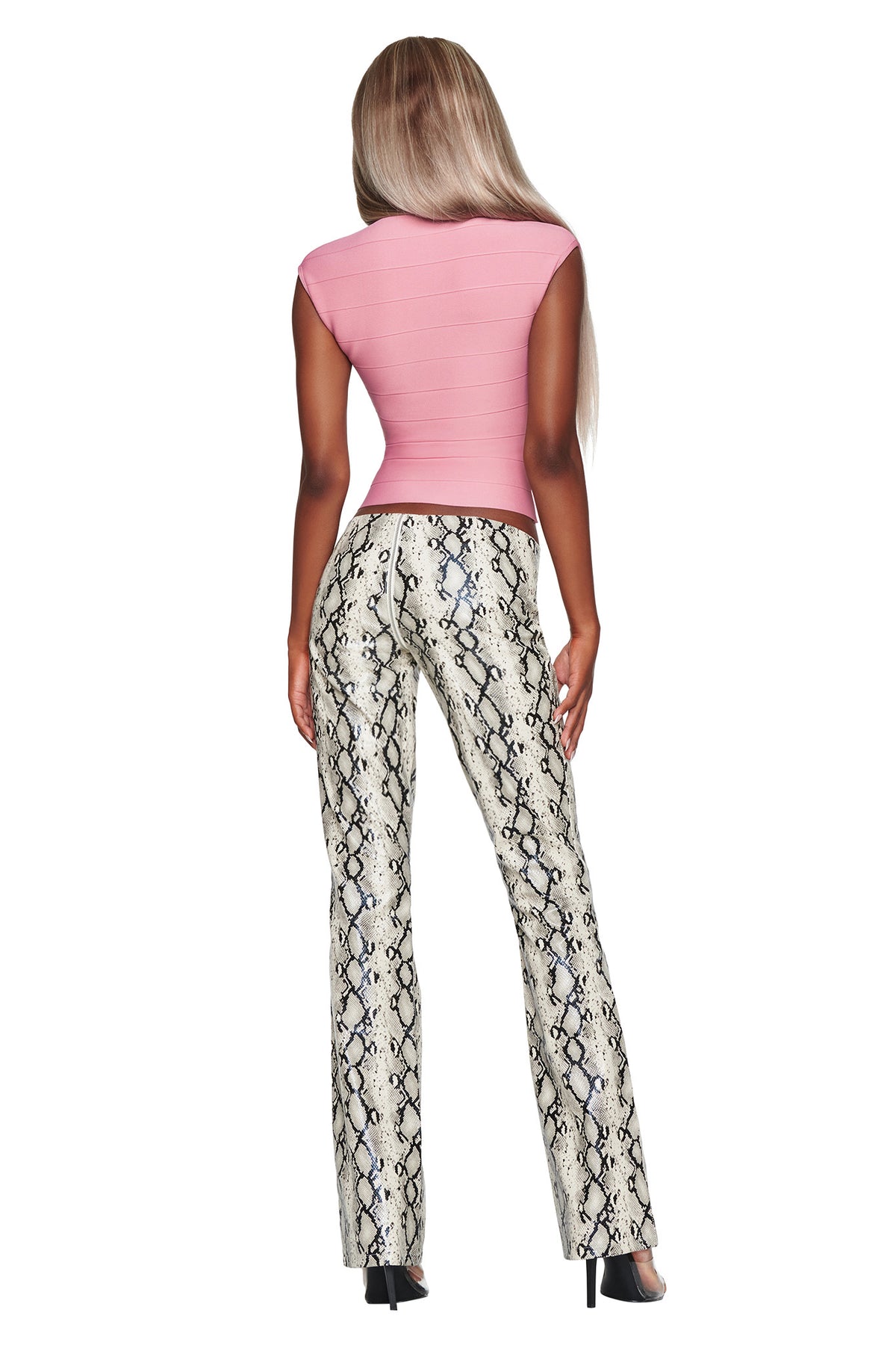 A person with long, straight hair is wearing a pink fitted top, the I.AM.GIA HENDRIX 2.0 PANT in Cream Snake, and black high-heeled shoes, standing with their back to the camera.