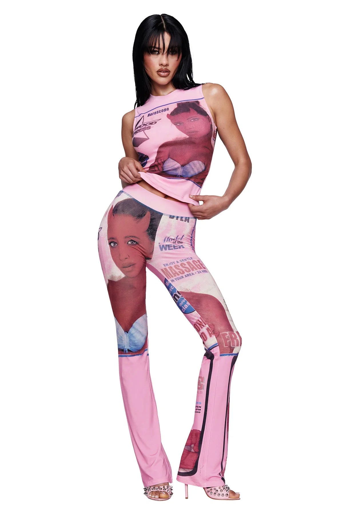 A woman poses in a matching pink outfit featuring the I.AM.GIA T-REX COURTNEY TANK with a placement print of faces and text. She wears open-toe heels, has straight dark hair with bangs, and stands against a plain white background.