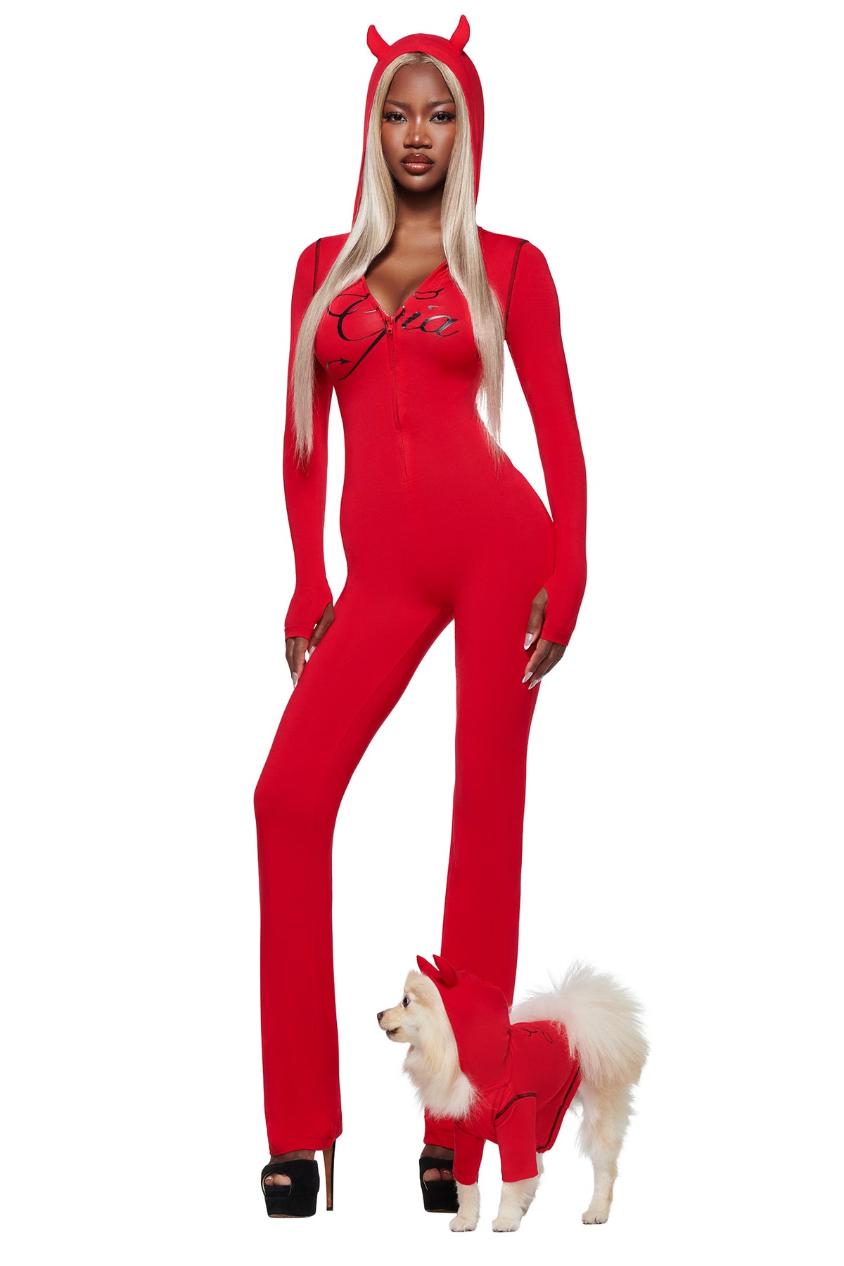 A woman wears the I.AM.GIA BLARE HORN JUMPSUIT - RED, standing beside a small dog dressed in a matching red hoodie.