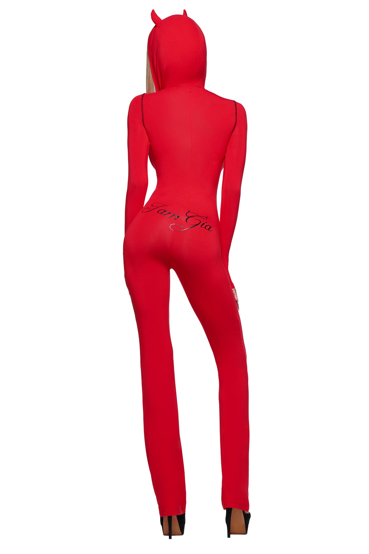 A figure stands with their back to the camera in the BLARE HORN JUMPSUIT - RED by I.AM.GIA, featuring a devil horn hood, black script on the back, and sleek black high heels.