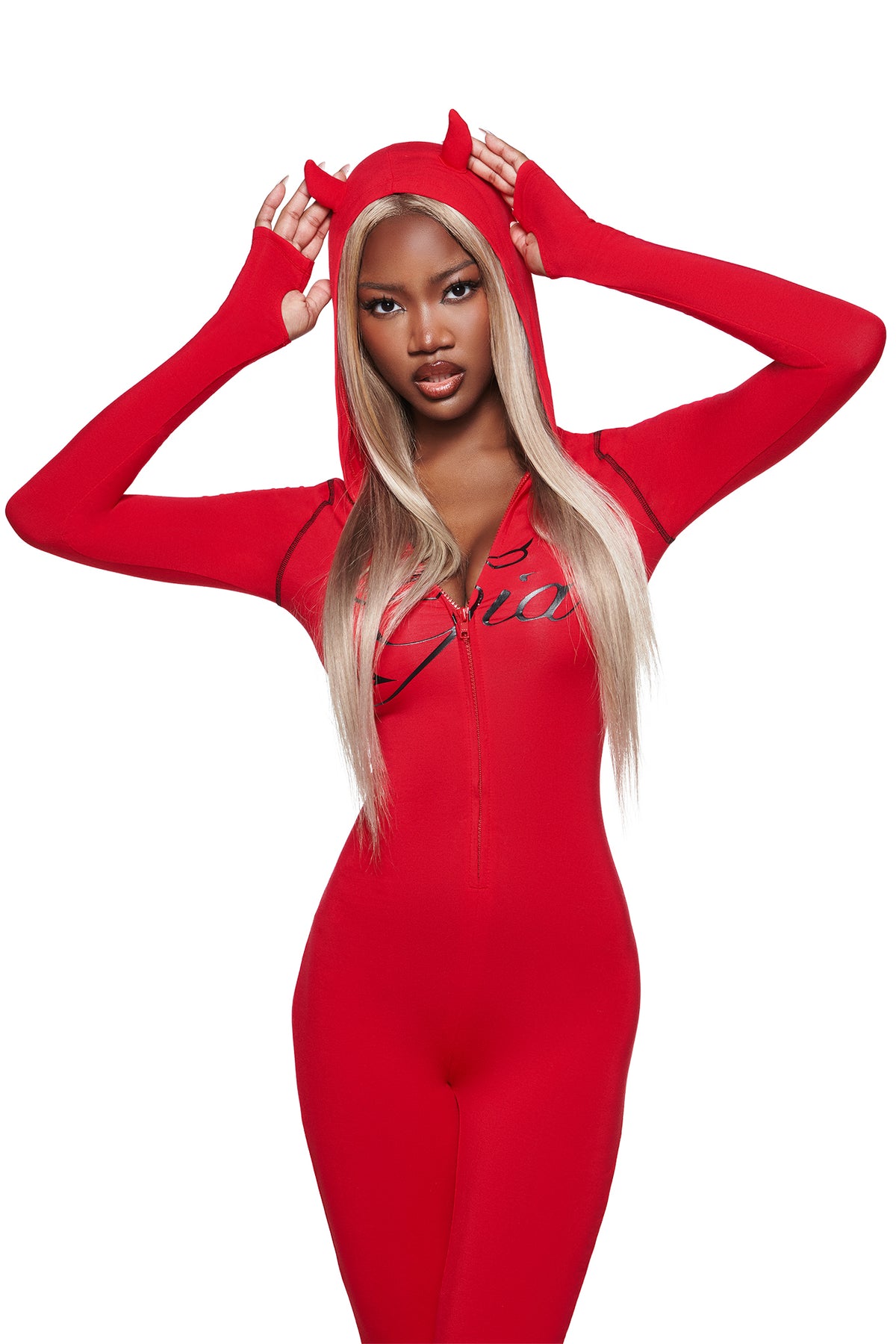 A woman in the BLARE HORN JUMPSUIT - RED by I.AM.GIA poses against a white background, her long blonde hair showing as she holds the devil horn hood with both hands.