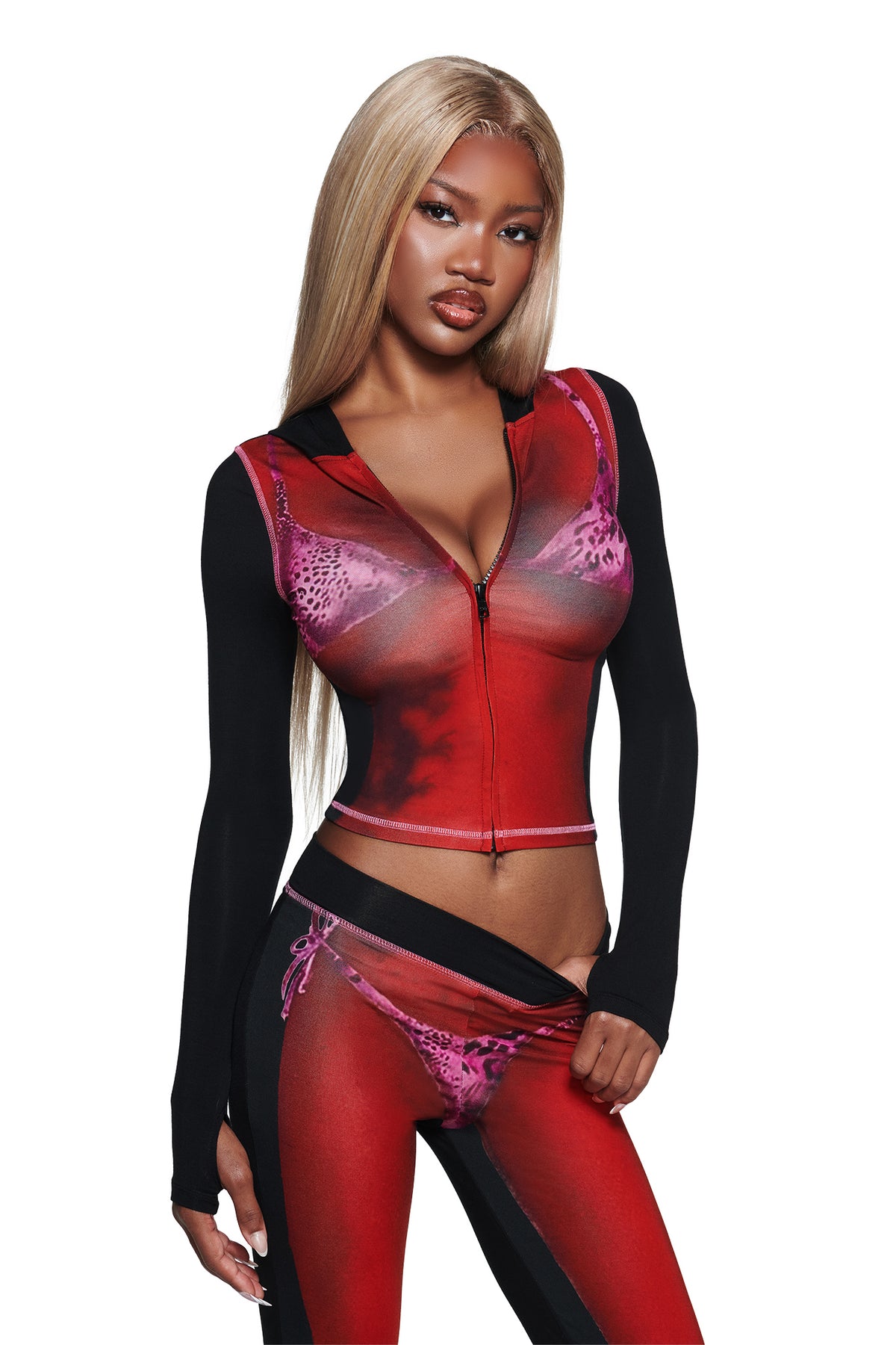 A woman with long straight blonde hair wears the I.AM.GIA T-REX SPRAY BODY BLARE HOODIE - BLACK, which features an airbrushed bikini body print. She stands against a white background, gazing at the camera neutrally.