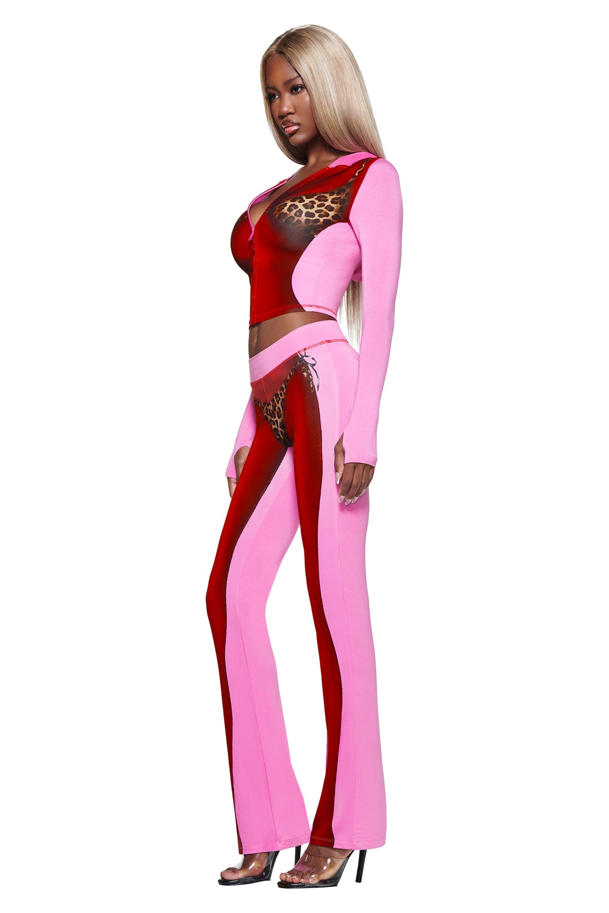 A woman with long blonde hair wears the I.AM.GIA T-REX SPRAY BODY BLARE HOODIE - PINK, styled with flared pants and high heels, posing against a white background.