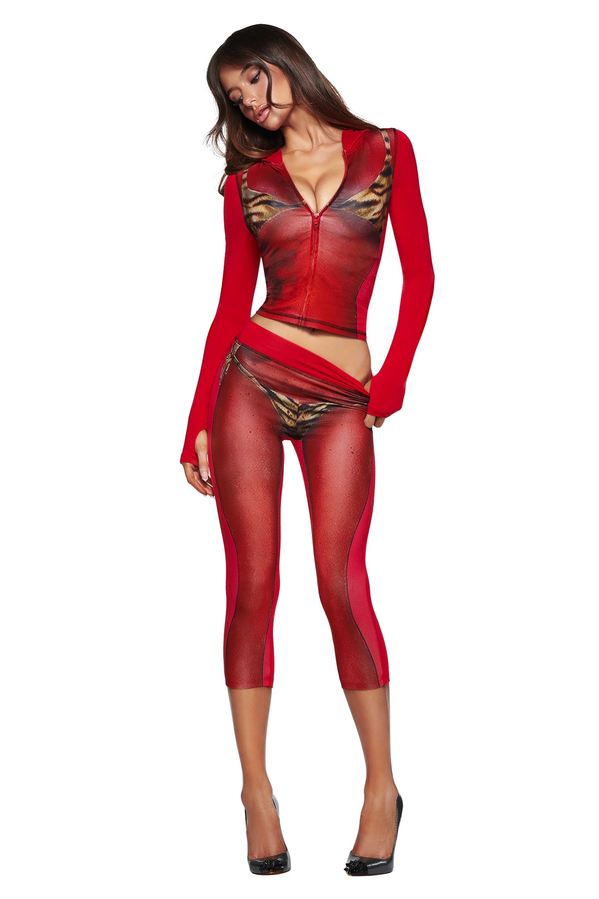 A woman poses against a white background in a red, sheer, form-fitting outfit with tiger print details and T-REX SPRAY BODY BLARE CAPRI - RED by I.AM.GIA, paired with black high heels.