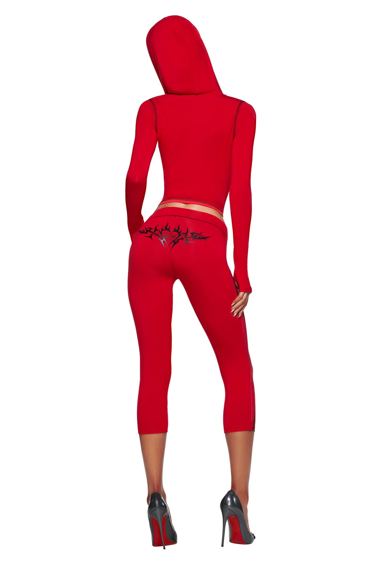 A person wears the T-REX SPRAY BODY BLARE HOODIE - RED by I.AM.GIA with matching red capri leggings, airbrushed bikini print, and black heels, standing back-facing on a white background.