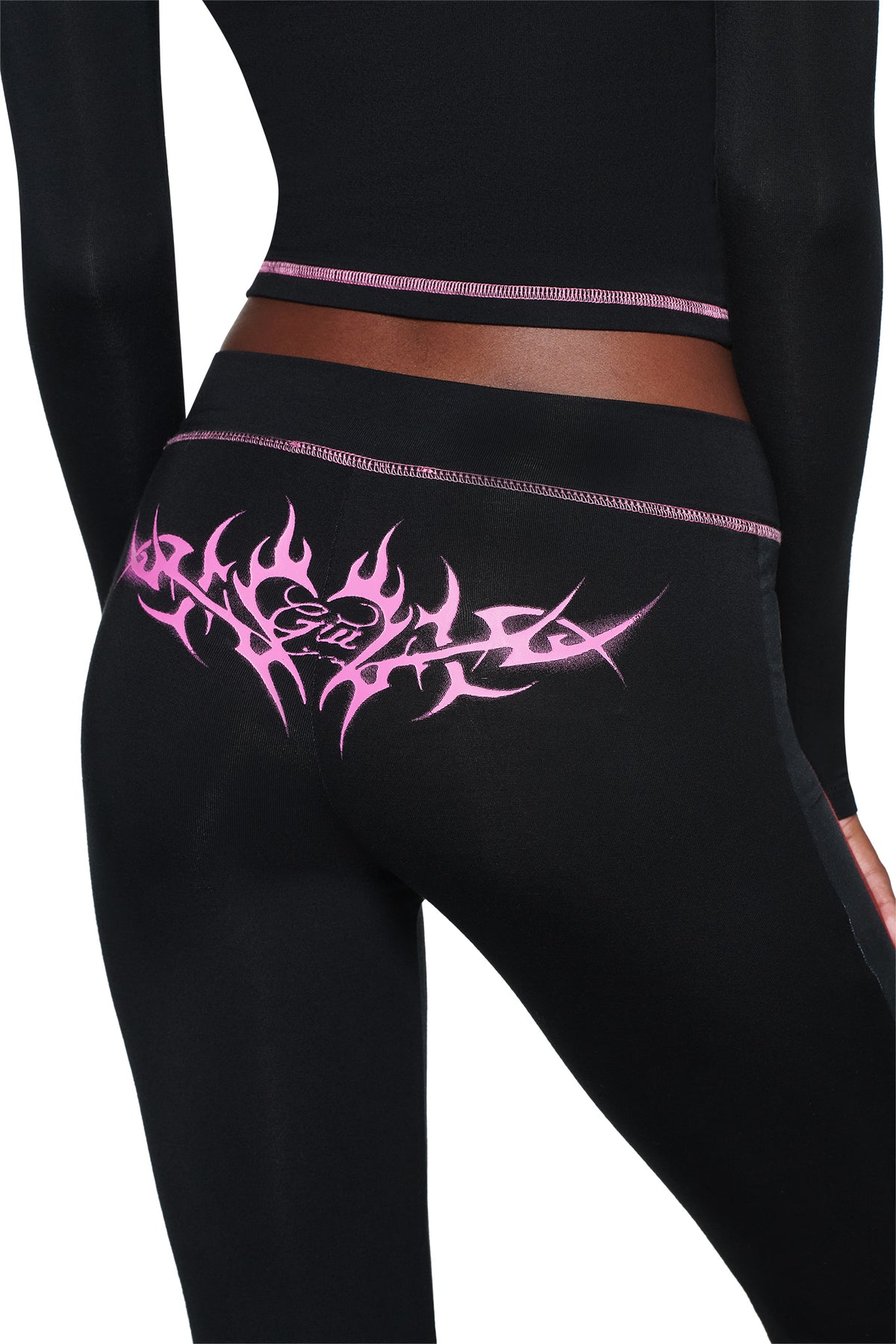 A person wearing I.AM.GIA T-REX SPRAY BODY BLARE TRACKPANT - BLACK with a pink flame design and “Girl” on the back, shown from behind against a white background.