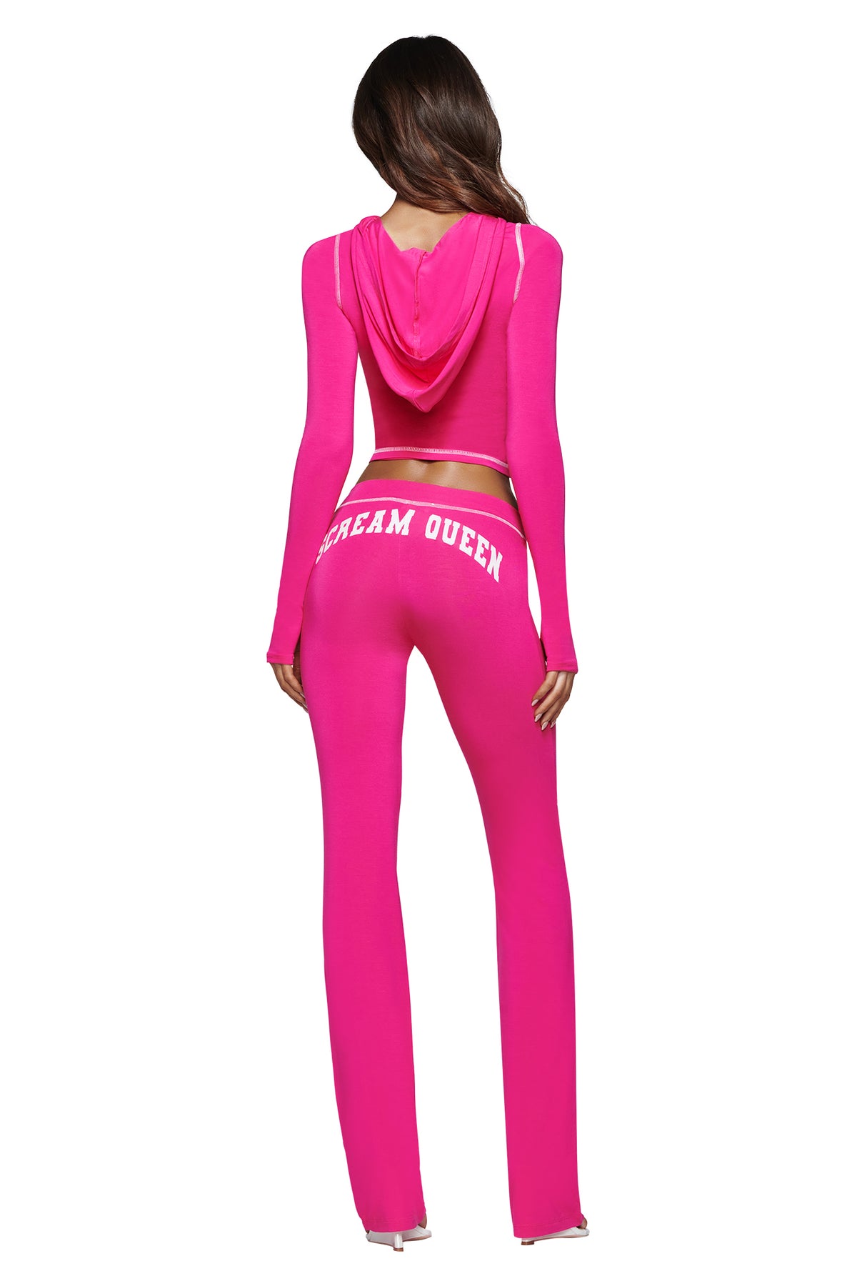 A woman stands with her back to the camera, wearing the I.AM.GIA BLARE TRACKPANT - HOT PINK SCREAM QUEEN and a matching hot pink hooded crop top. “SCREAM QUEEN” is printed in white on the back of the pants.