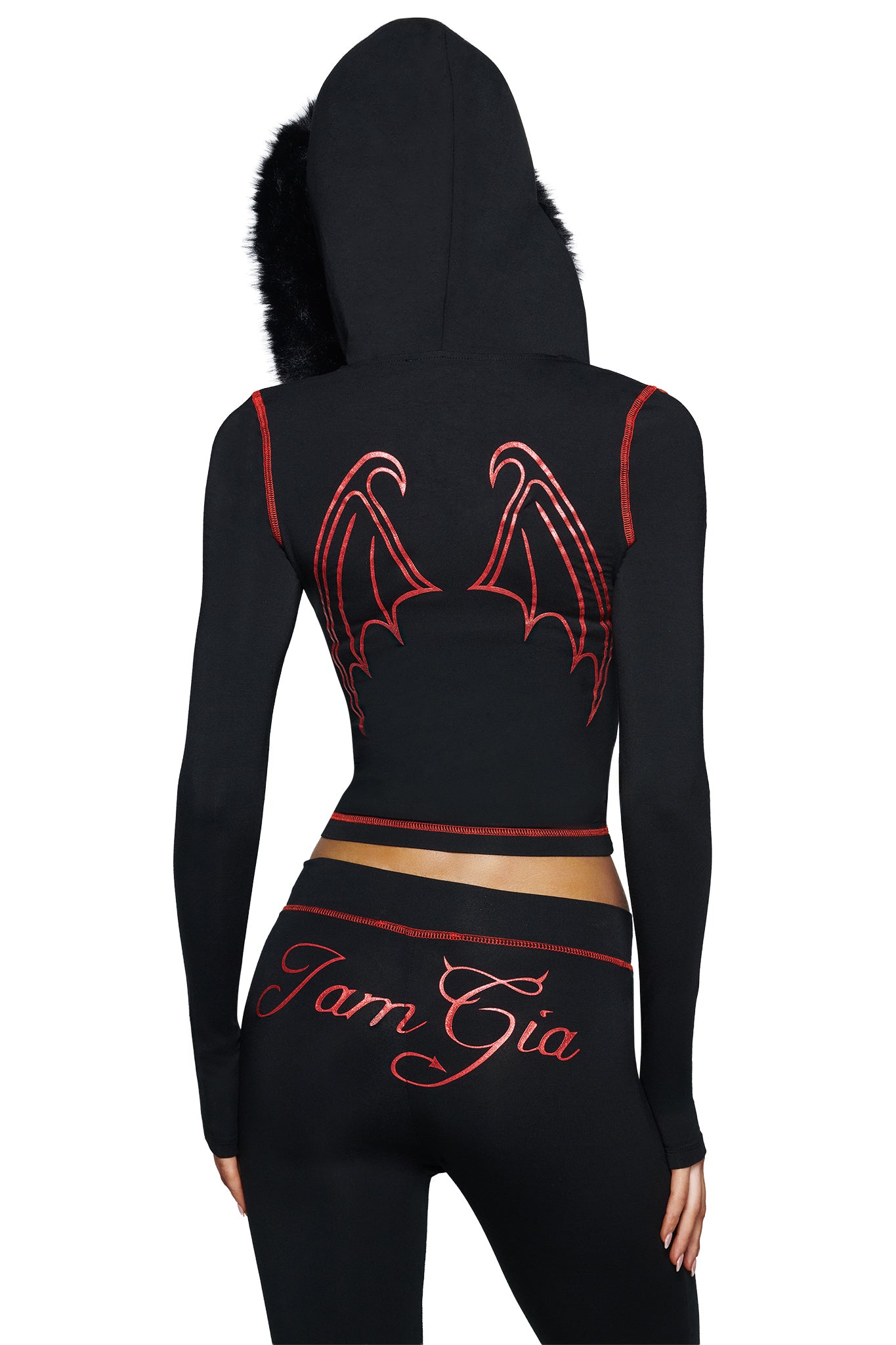 A person is seen from behind wearing the I.AM.GIA BLARE TRACKPANT - JET BLACK : DEVIL, a black hooded outfit accented by red-trimmed bat wings on the back and finished with “I.AM.GIA” in bold red script on the waistband. The look showcases signature Blare Trackpant styling and features the striking devil GIA logo for an edgy statement.