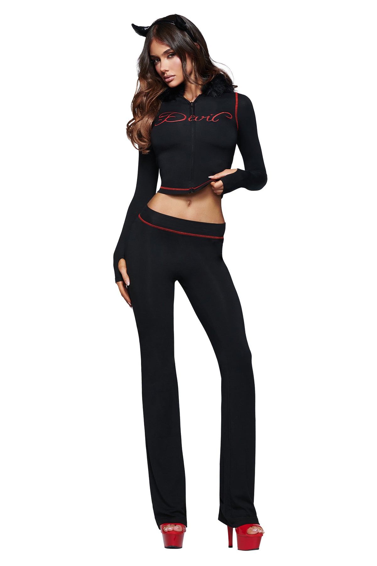 A woman poses against a white background wearing the I.AM.GIA BLARE TRACKPANT - JET BLACK : DEVIL, paired with a black crop top, red high heels, and a black devil horns headband featuring the GIA logo.