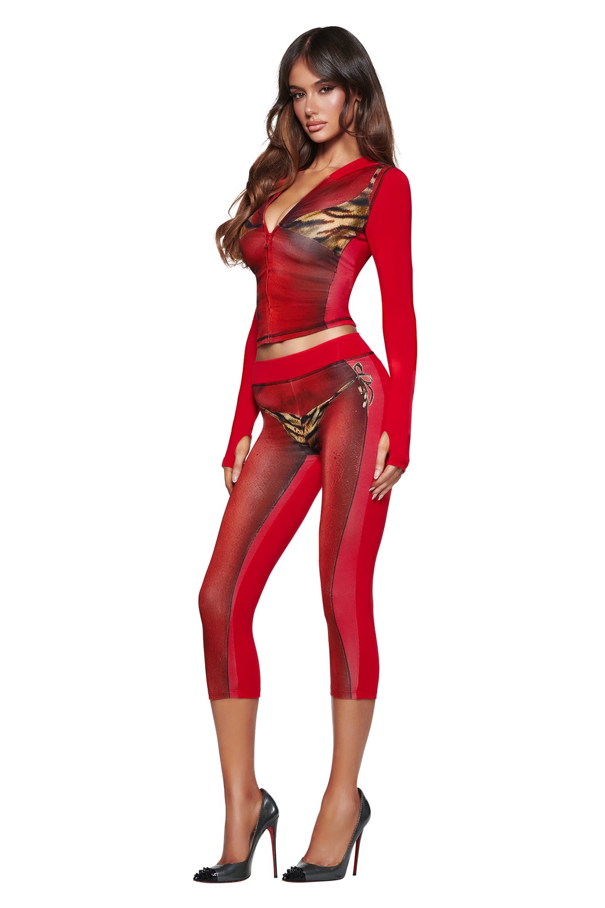 A woman poses in the I.AM.GIA T-REX SPRAY BODY BLARE CAPRI - RED, a fitted red and gold three-quarter length outfit, paired with black heels, against a white background.