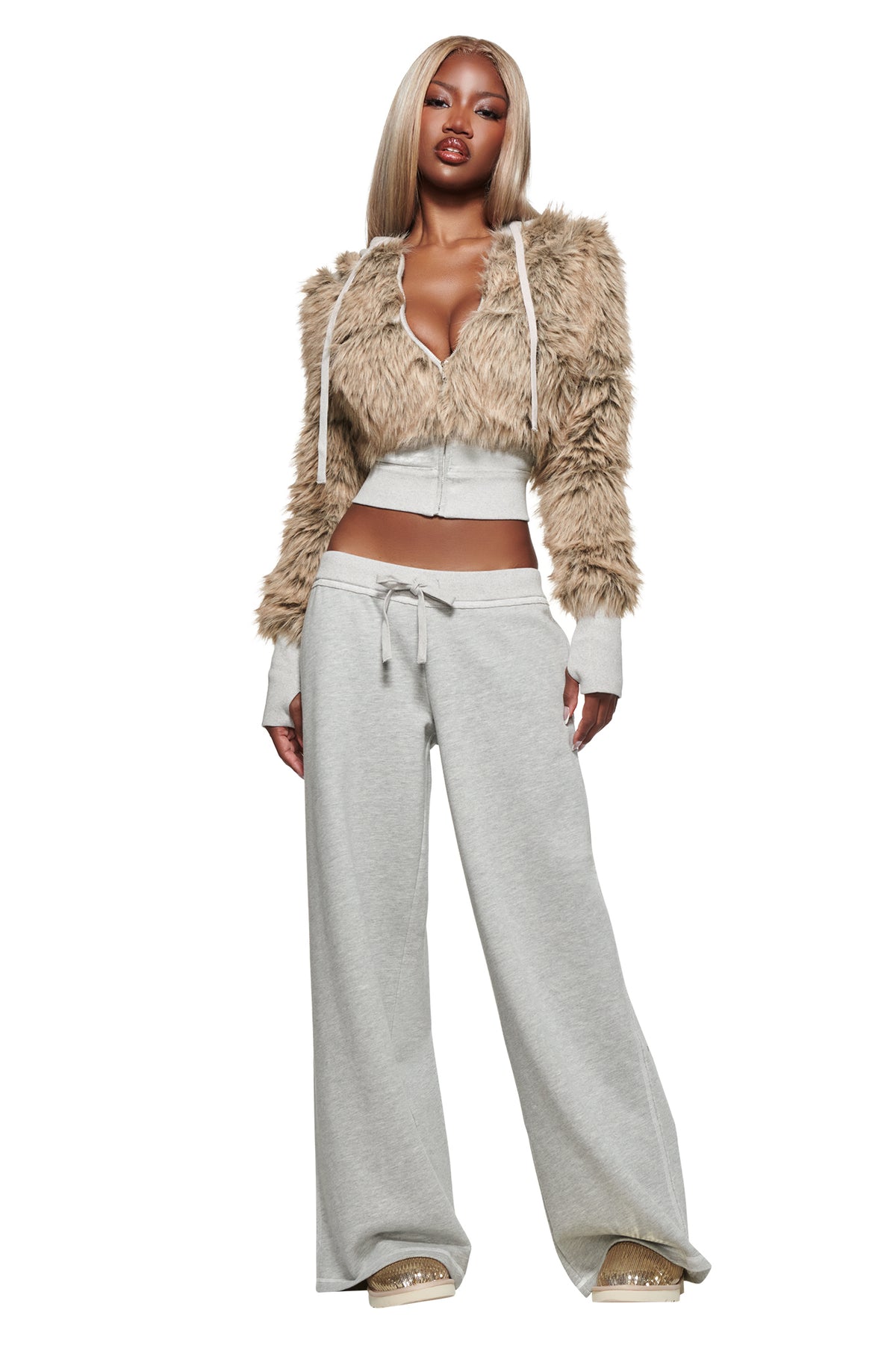A woman poses against a white background wearing the I.AM.GIA KOKO TRACKPANT in heather grey—a light gray, low-rise, wide-leg style crafted from soft French terry—paired with a tan faux fur cropped jacket and beige sandals.