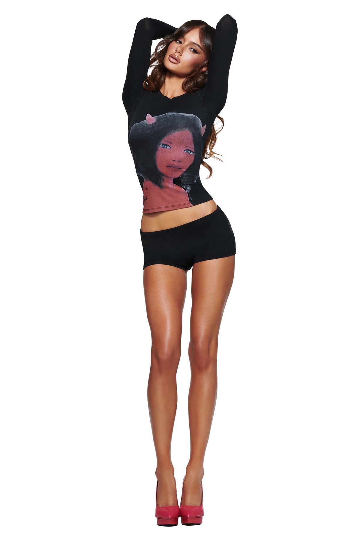 A woman in a black long-sleeve cartoon graphic shirt and I.AM.GIA T-REX BLARE 2.0 SHORT - BLACK poses with raised arms and pink heels against a white background.