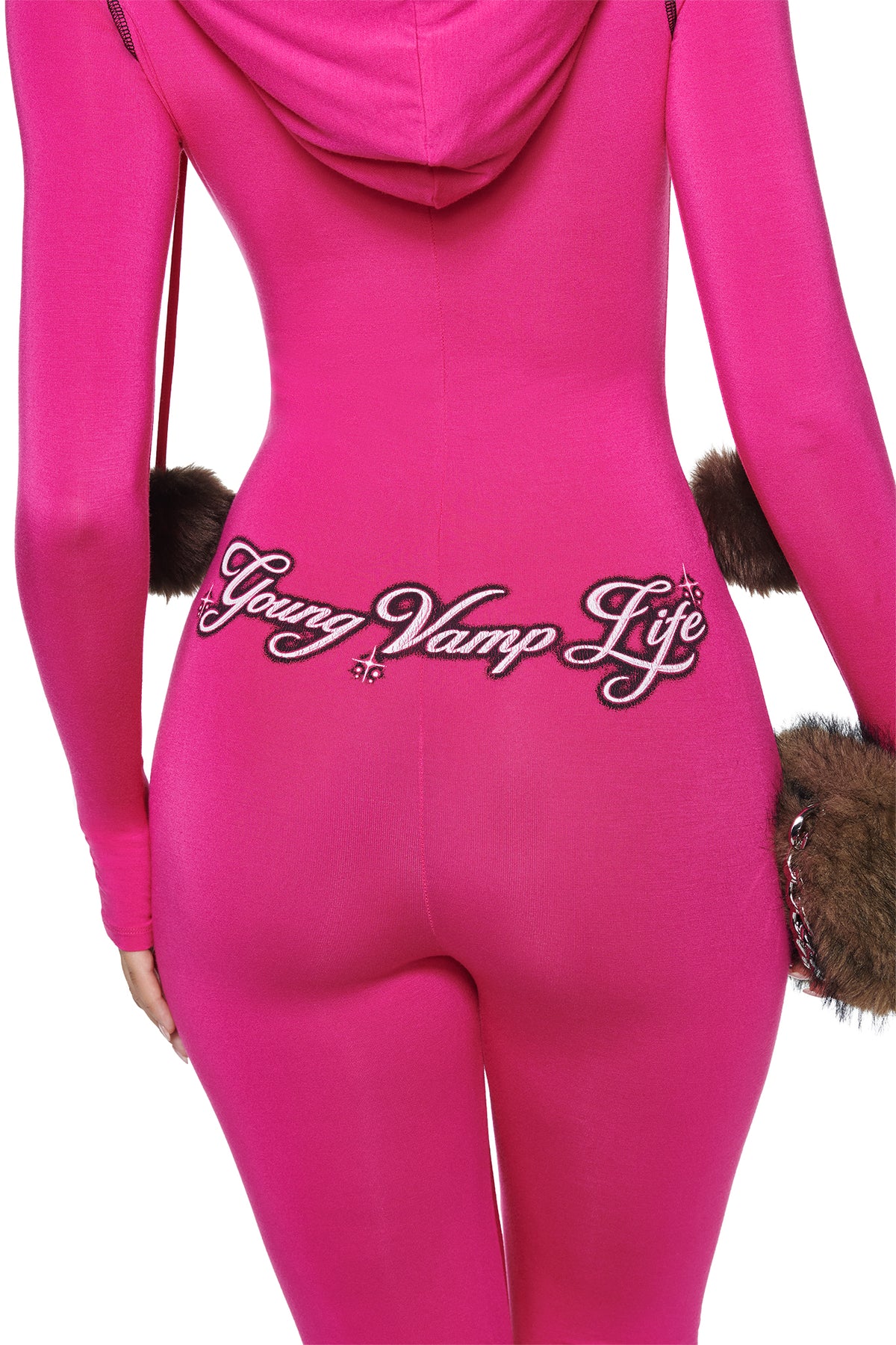 Back view of the YVL BLARE FUR LINED JUMPSUIT - PINK, a hot pink jumpsuit with a faux fur hood, “Young Vamp Life” embroidered in script across the lower back, and brown faux fur trim at the cuffs and waist.