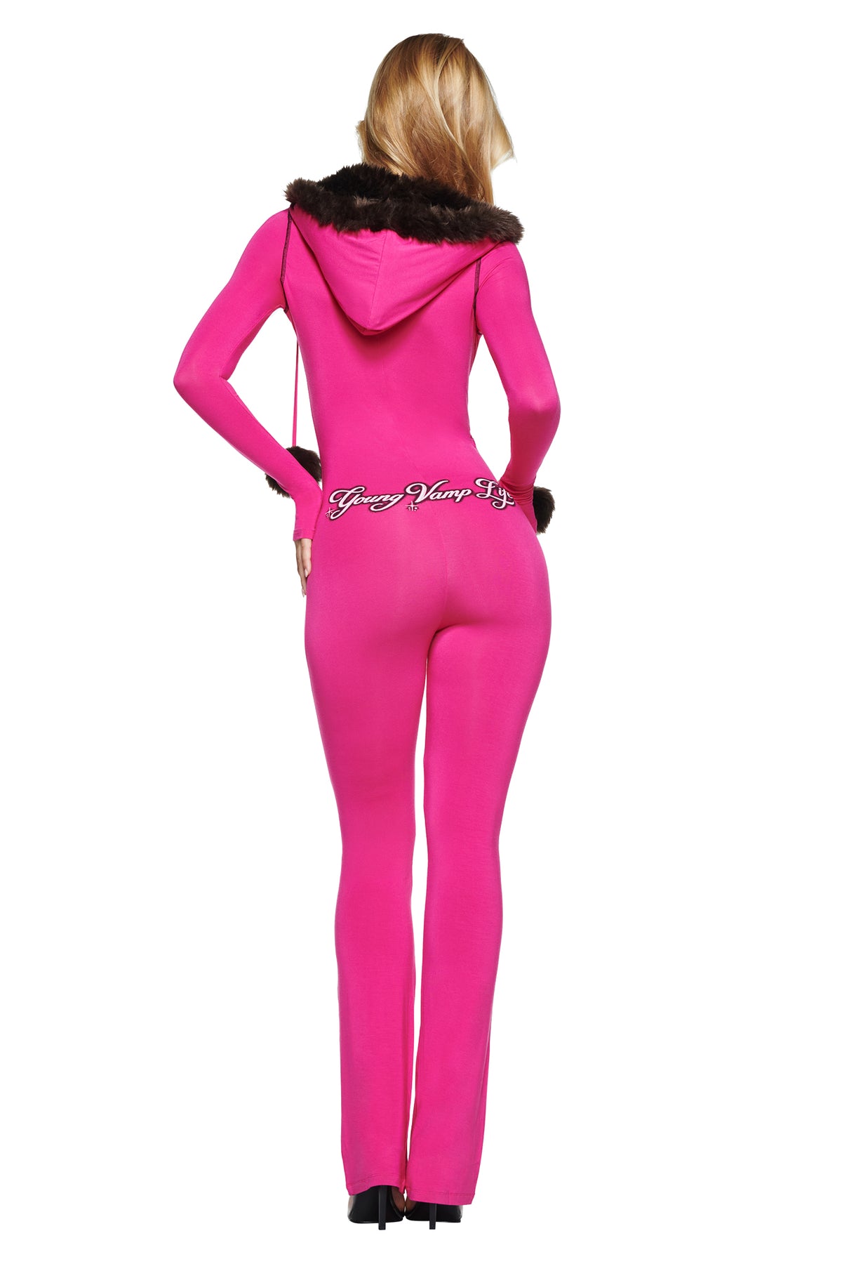 A person wearing a bright pink I.AM.GIA YVL BLARE FUR LINED JUMPSUIT with flare leg pants and a brown faux-fur trimmed hood, featuring the text “Young Vamp Lyf” on the lower back.