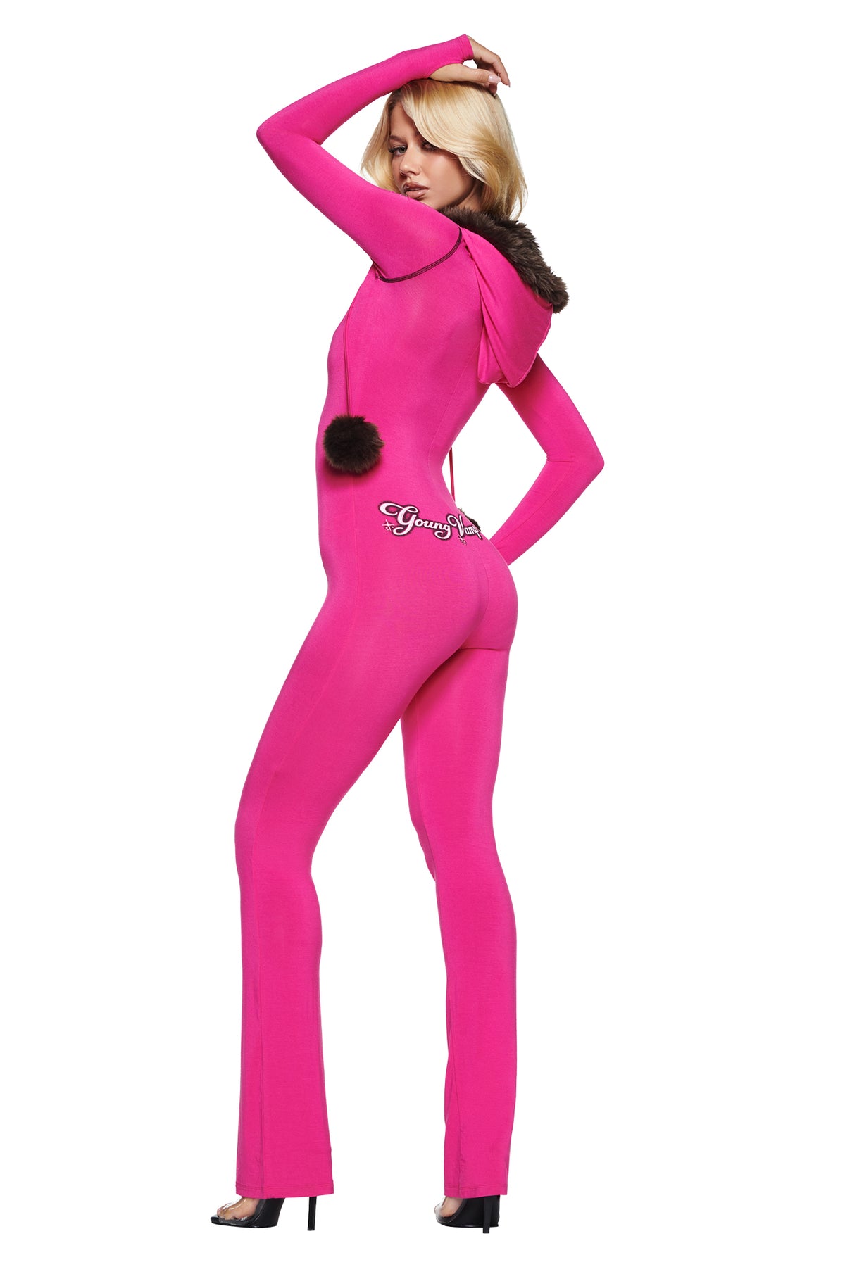 A woman wearing a pink YVL BLARE FUR LINED JUMPSUIT with a faux fur-trimmed hood and pom-pom detail on the back.