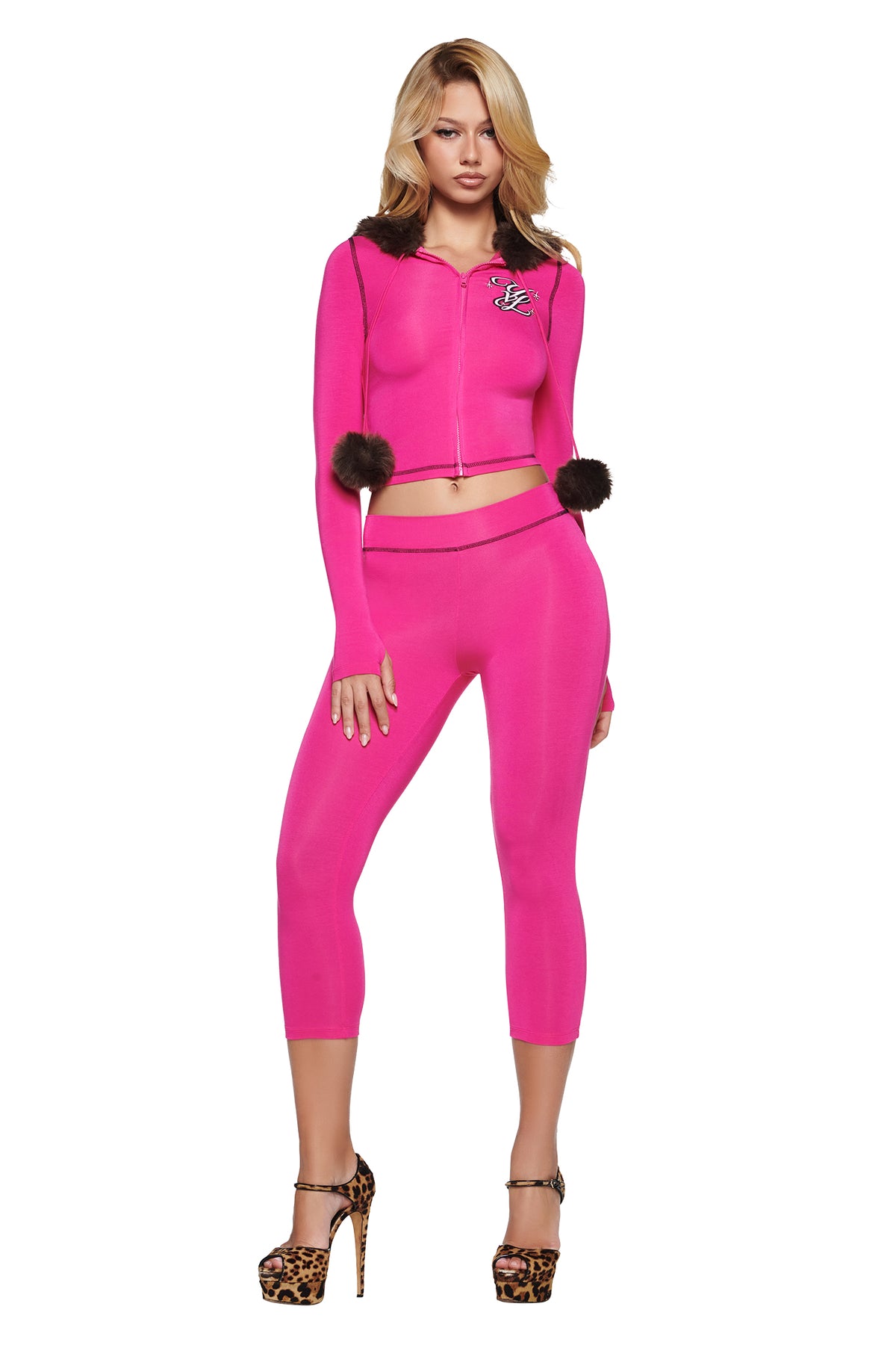 A person wears a hot pink YVL BLARE FUR LINED HOODIE with dark faux-fur trim and dangling pom-poms, paired with matching pink cropped leggings and leopard-print high-heeled sandals.