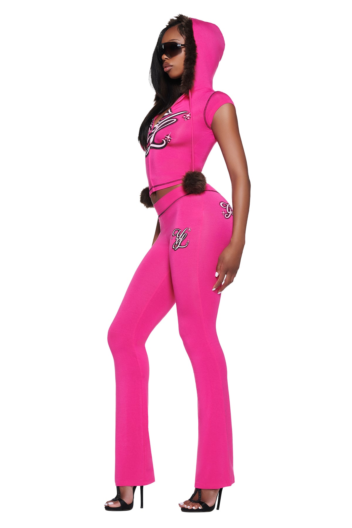 A person wearing a bright pink hooded short-sleeve top and matching YVL BLARE TRACKPANT - PINK with embroidered logos and brown fur accents.