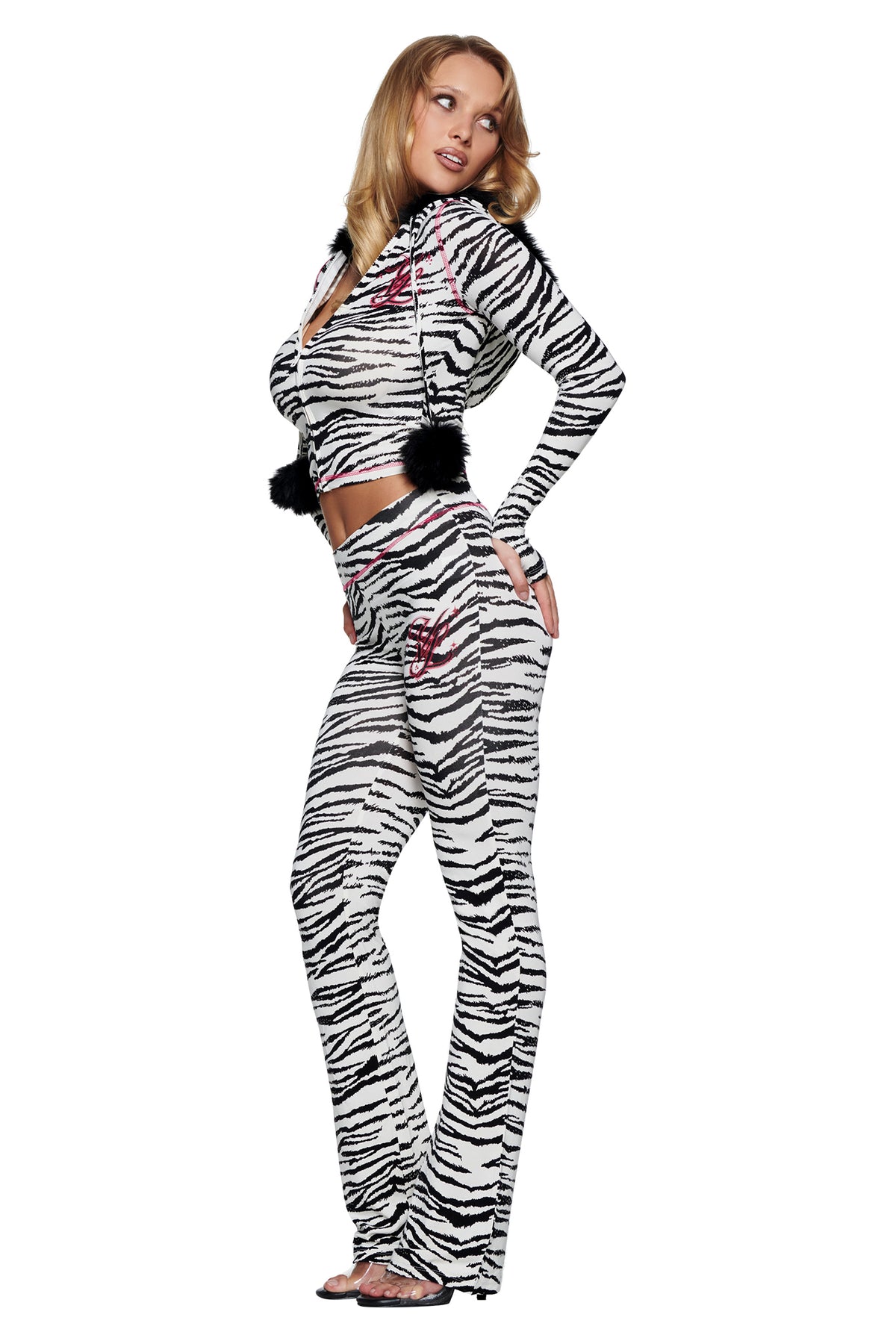 A model wears a zebra-print long-sleeved cropped zip-up hoodie with black pom-poms and matching YVL BLARE TRACKPANT - ZEBRA.