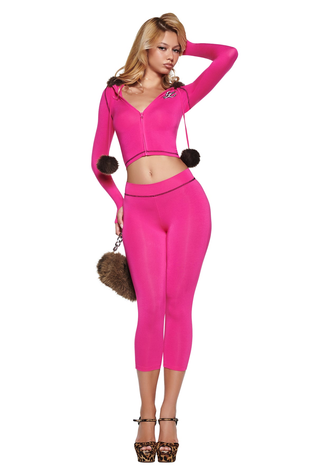 A woman wears a bright pink cropped zip-up hoodie with fur pom-pom drawstrings and matching I.AM.GIA YVL BLARE CAPRI - PINK pants, paired with leopard-print platform heels and a brown fur handbag.