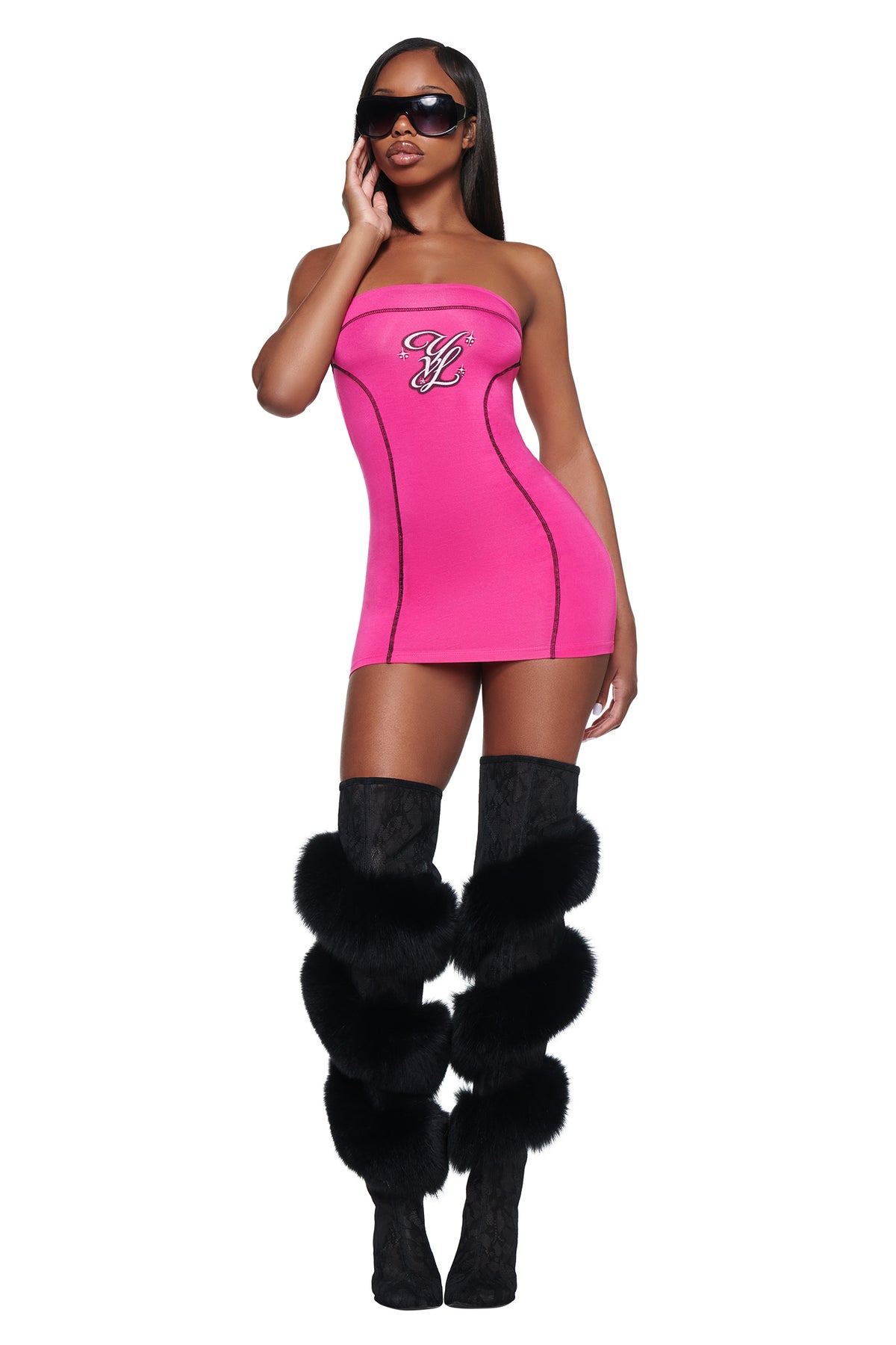 A woman wears a bright pink I.AM.GIA YVL BLARE TUBE MINI DRESS in bamboo fabric with a logo on the chest, paired with black fur-trimmed thigh-high boots.