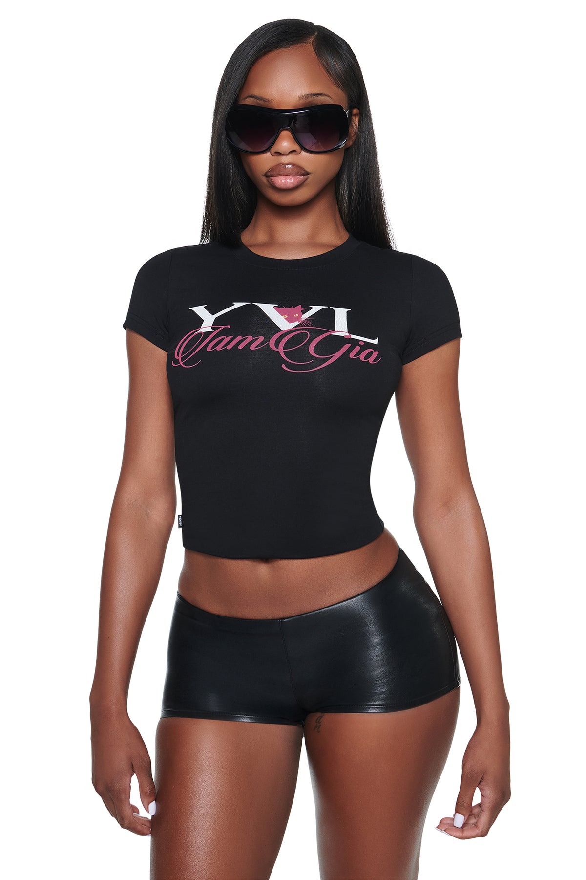 A person wearing a black cropped YVL T-SHIRT - BLACK CAT featuring “YVL” branding and a small pink cat illustration.