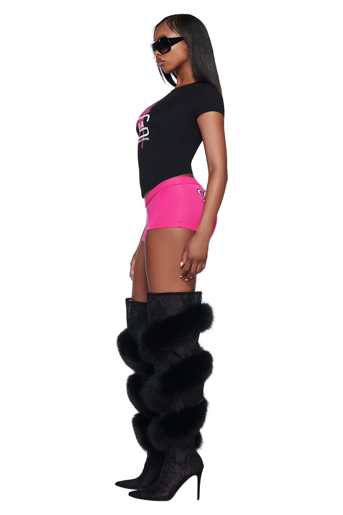 A woman in profile wearing a black YVL T-SHIRT - BLACK GIA, pink shorts, and knee-high boots with black fur trim.