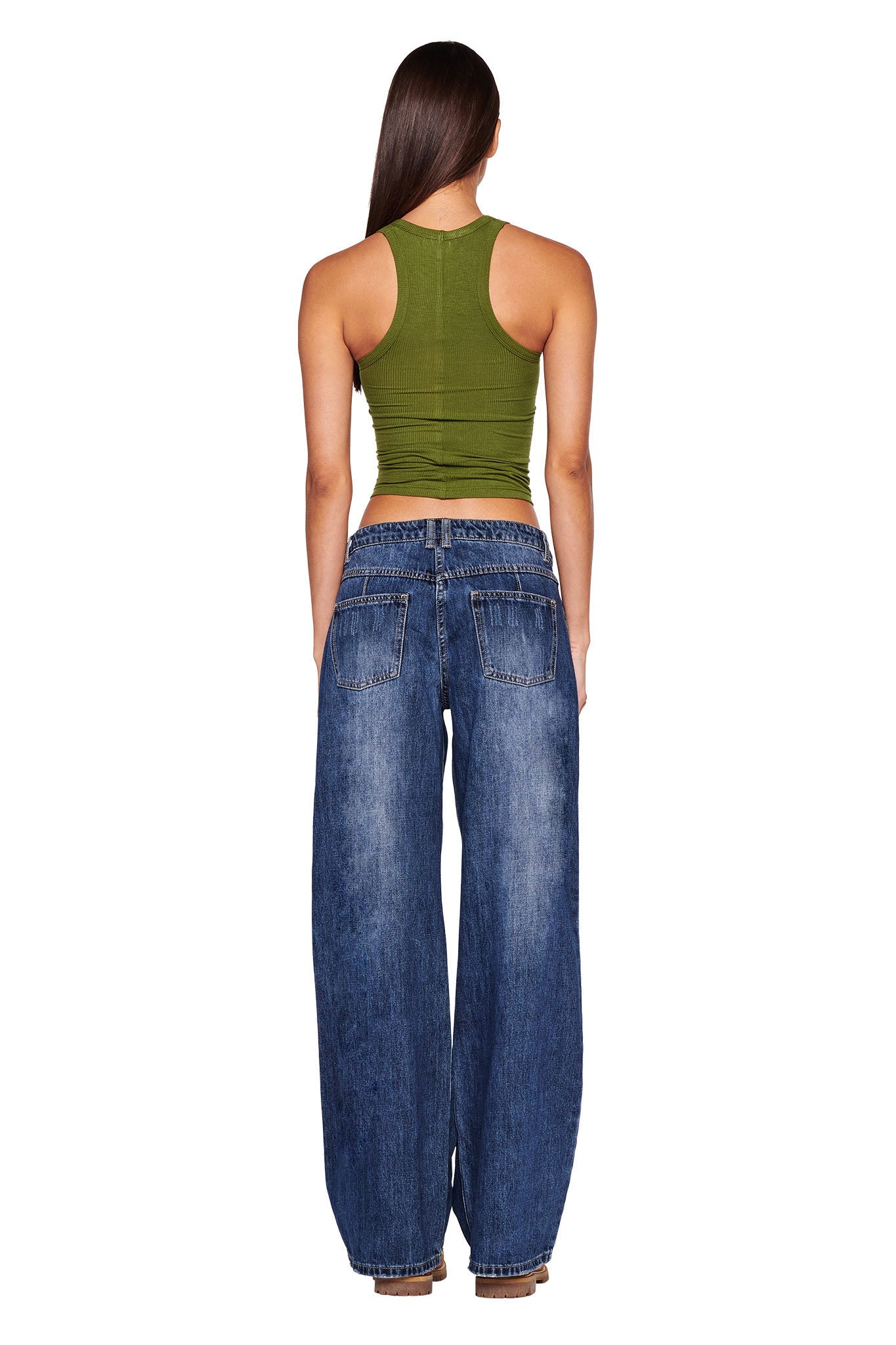 A person with long dark hair stands facing away from the camera, wearing a fitted, sleeveless green top from I.AM.GIA and the DYLAN JEAN - DARK BLUE from I.AM.GIA. The background is white.