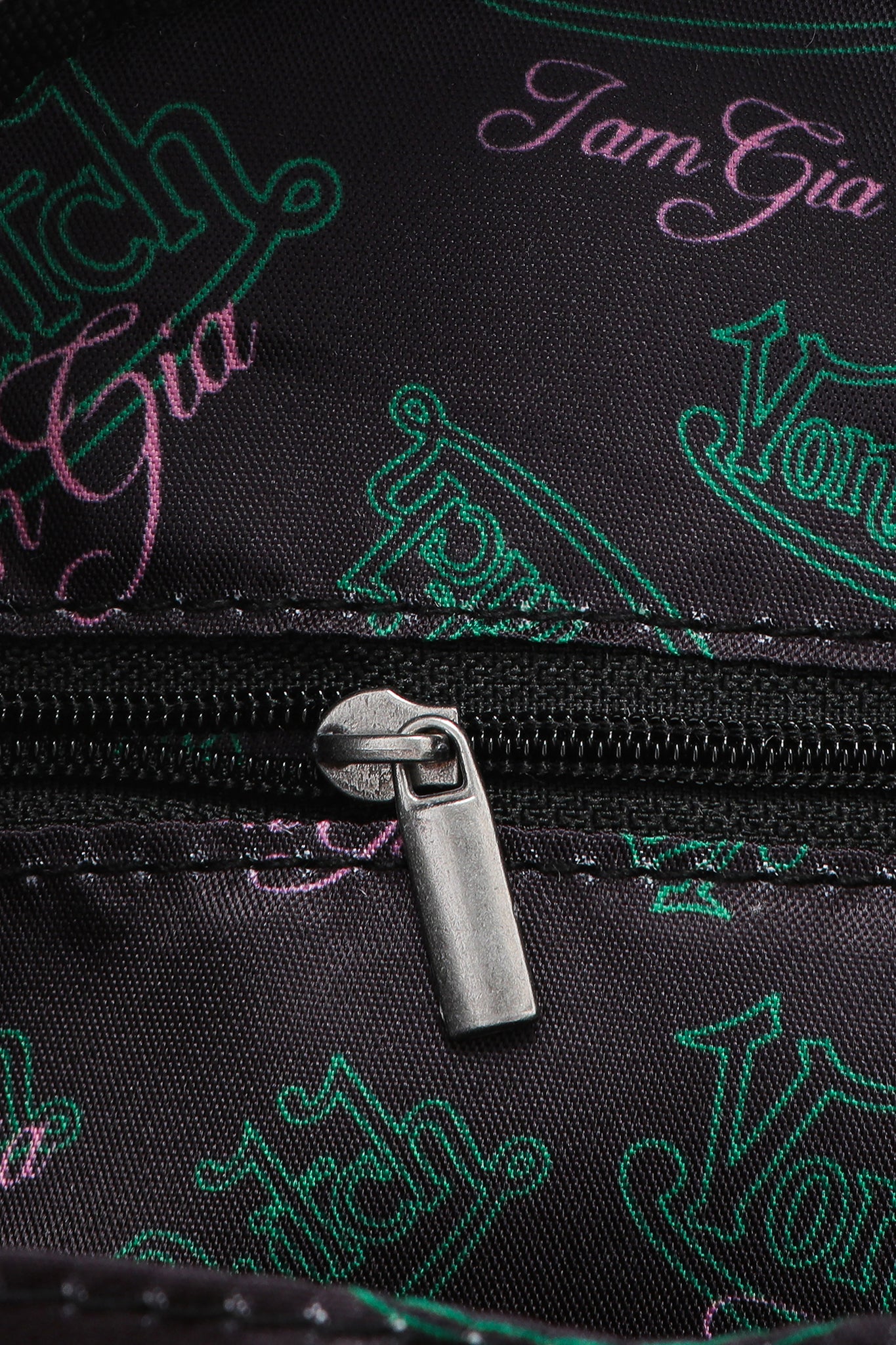 A close-up of the I.AM.GIA X VON DUTCH MINI BOWLING BAG - LEOPARD shows a metallic zipper on black fabric with green and pink logos, perfect for fans of this exclusive I.AM.GIA collaboration.