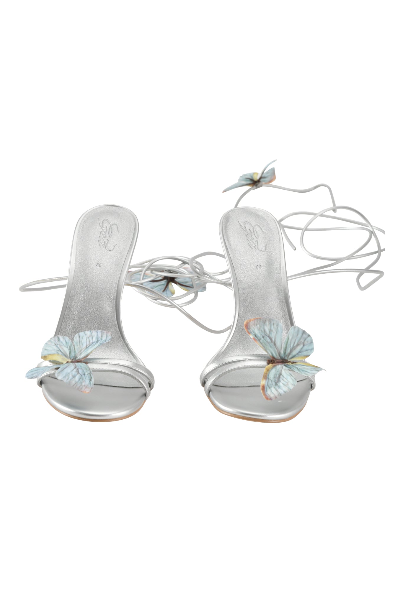 The SCARLETTE HEEL - SILVER by I.AM.GIA is a pair of silver metallic strappy stilettos with ankle straps and light blue butterfly appliques on the open toe and near the laces.