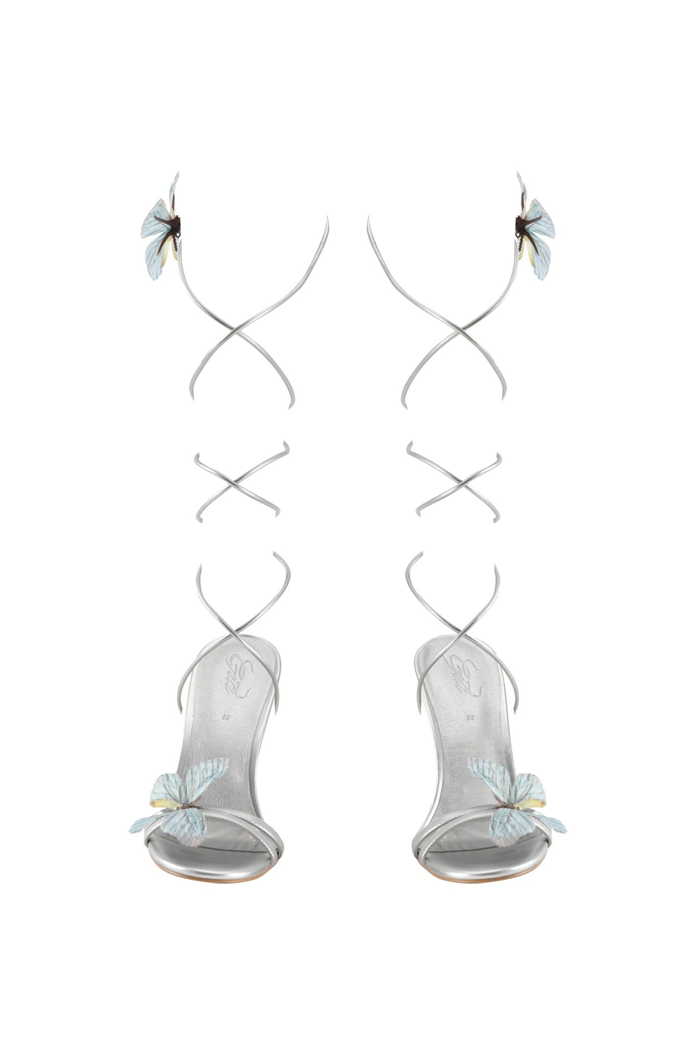 The SCARLETTE HEEL - SILVER by I.AM.GIA is an elegant pair of metallic strappy stilettos featuring thin crisscross ankle straps and delicate blue butterfly appliqués on the open toe, displayed on a white background.