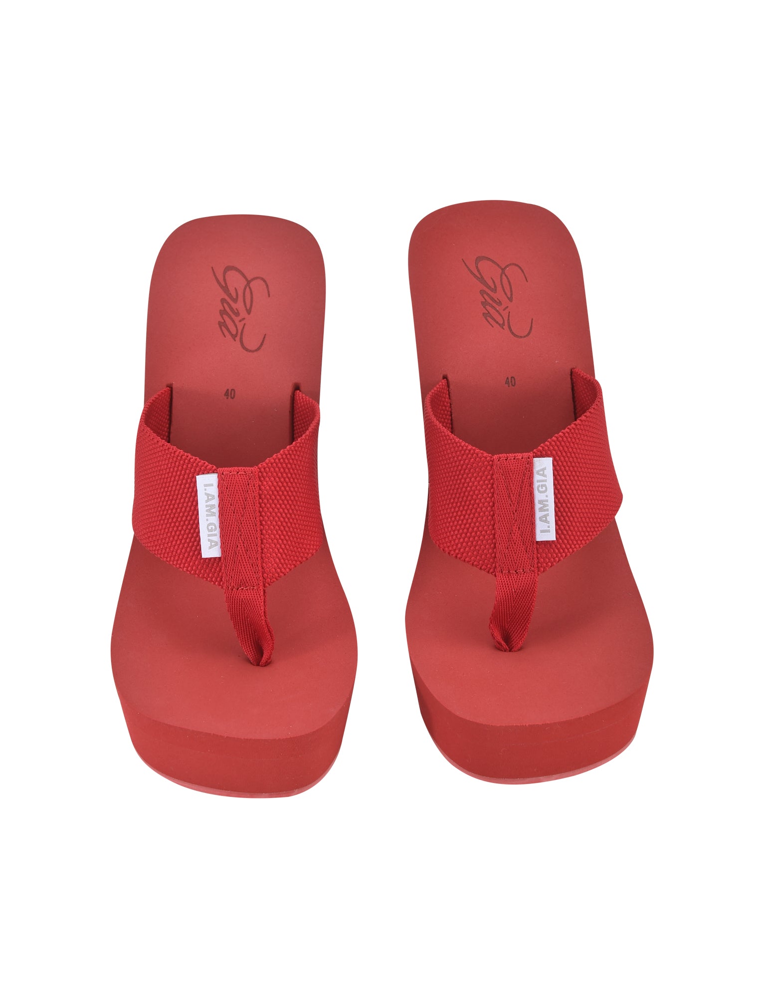 A pair of SHELBY FLIP FLOP - RED by I.AM.GIA, featuring thick, textured straps and elevated cushioned soles, is laid out side-by-side. The insole showcases cursive writing with the size number "40" indicated. Each strap includes a small white tag with text that subtly flaunts the I.AM.GIA brand essence.