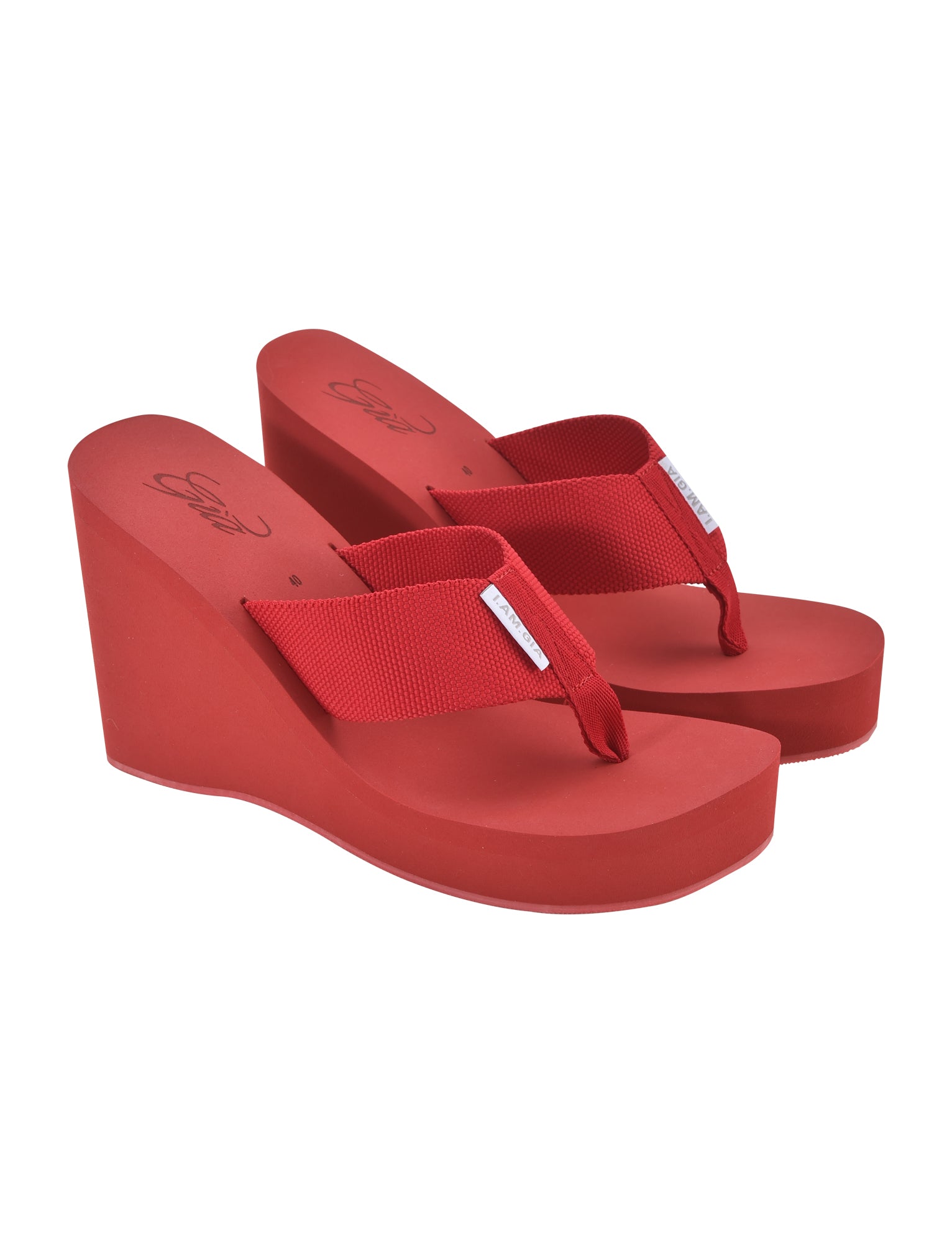 A pair of SHELBY FLIP FLOP sandals in red by I.AM.GIA, featuring thick wedge soles and fabric straps. Both sandals are positioned facing left, with the left one slightly ahead of the right. A small white tag labeled "I.AM.GIA" is attached to the straps, and the soles are embossed with brand logos.